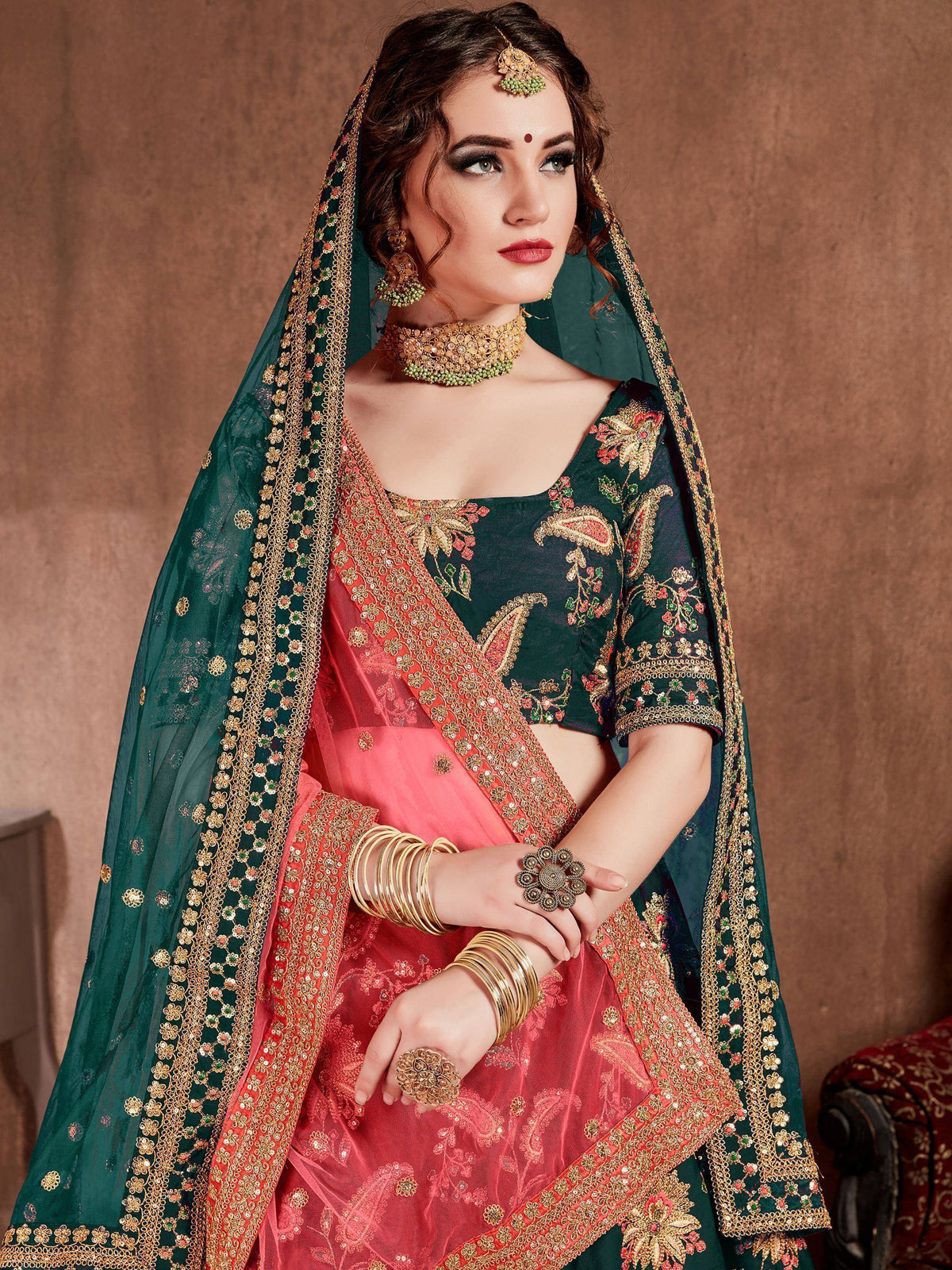 Emerald green and coral pink embroidered lehenga choli with gold detailing, perfect for Indian weddings and festive occasions.