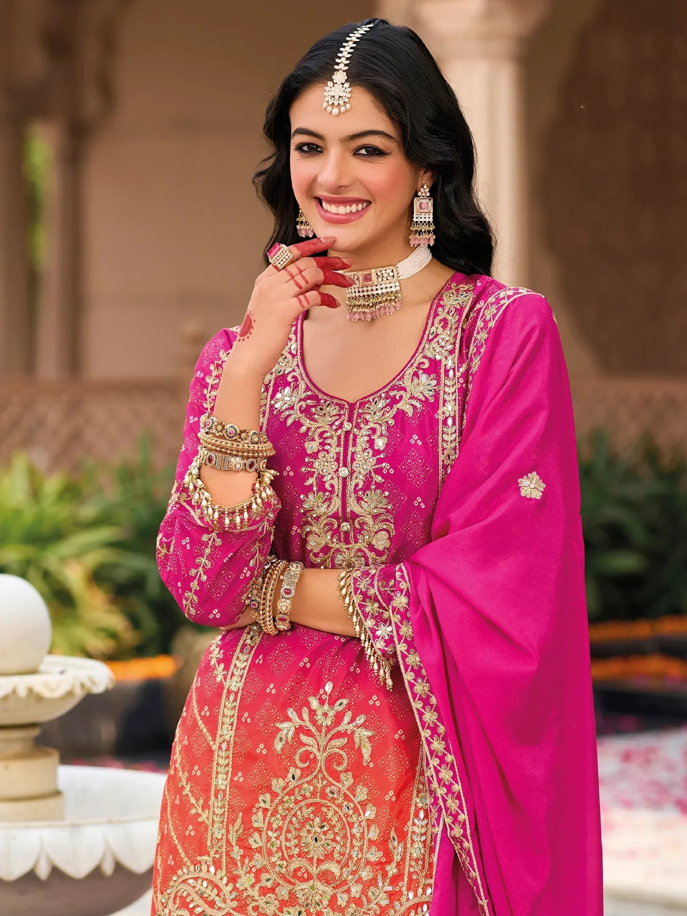 Woman in vibrant pink and orange embroidered Indian ethnic wear with gold jewelry and henna