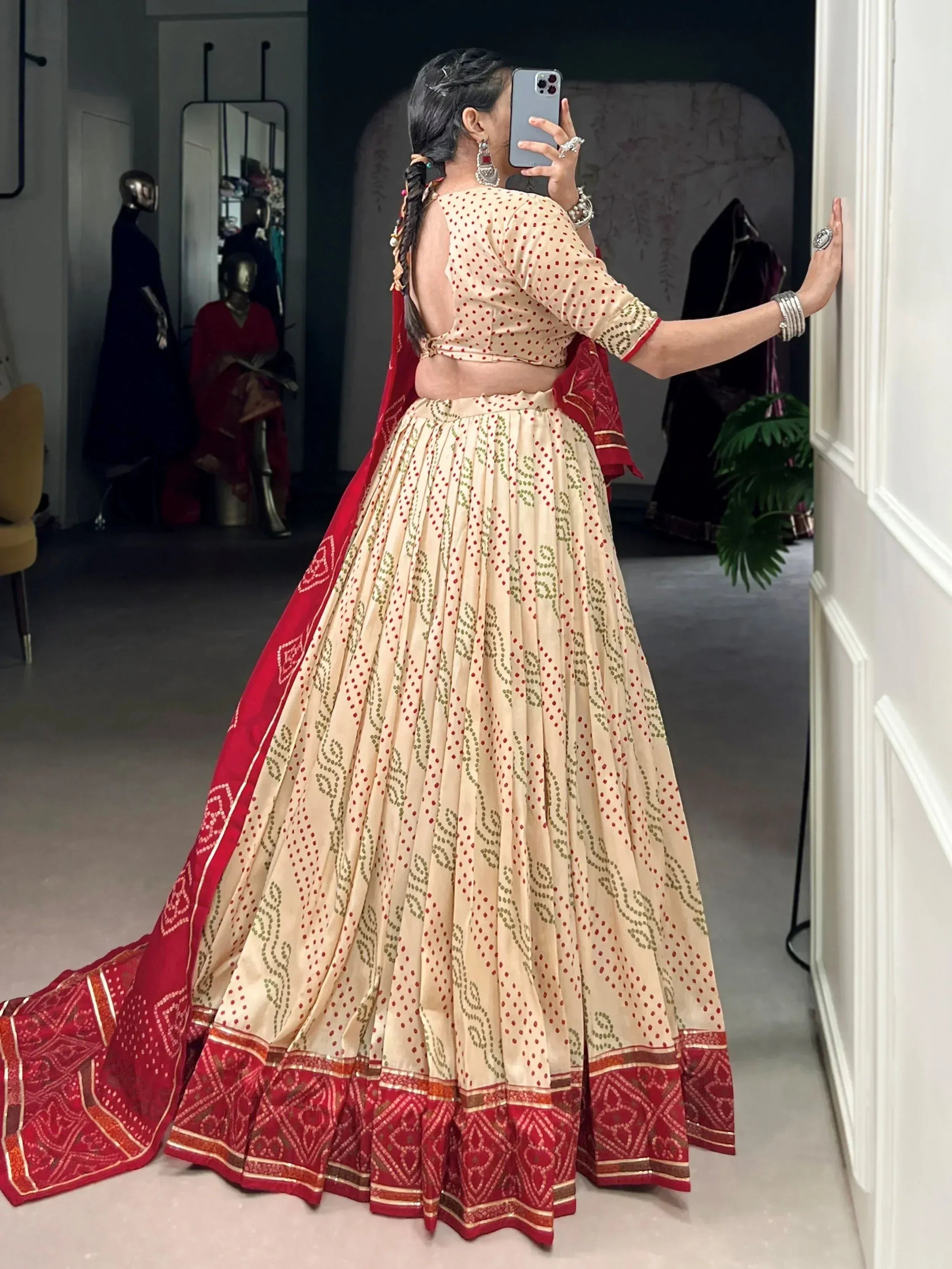 Woman in beige and red printed lehenga choli with backless blouse, taking mirror selfie in boutique