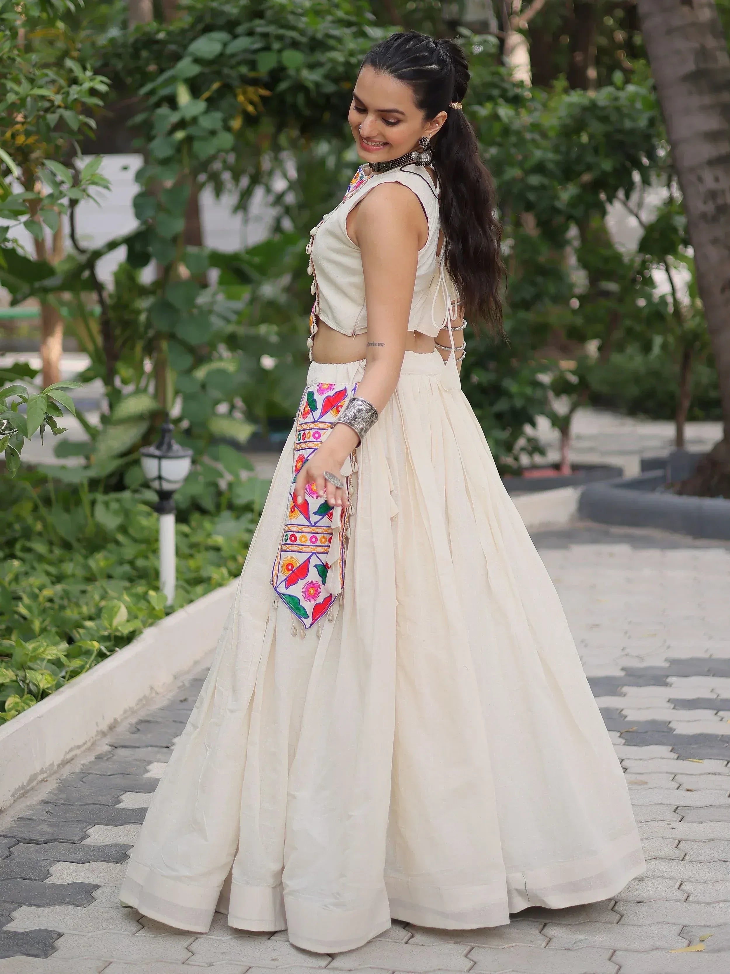 Woman in off-white embroidered lehenga choli with colorful mirror work, perfect for Indian ethnic occasions.