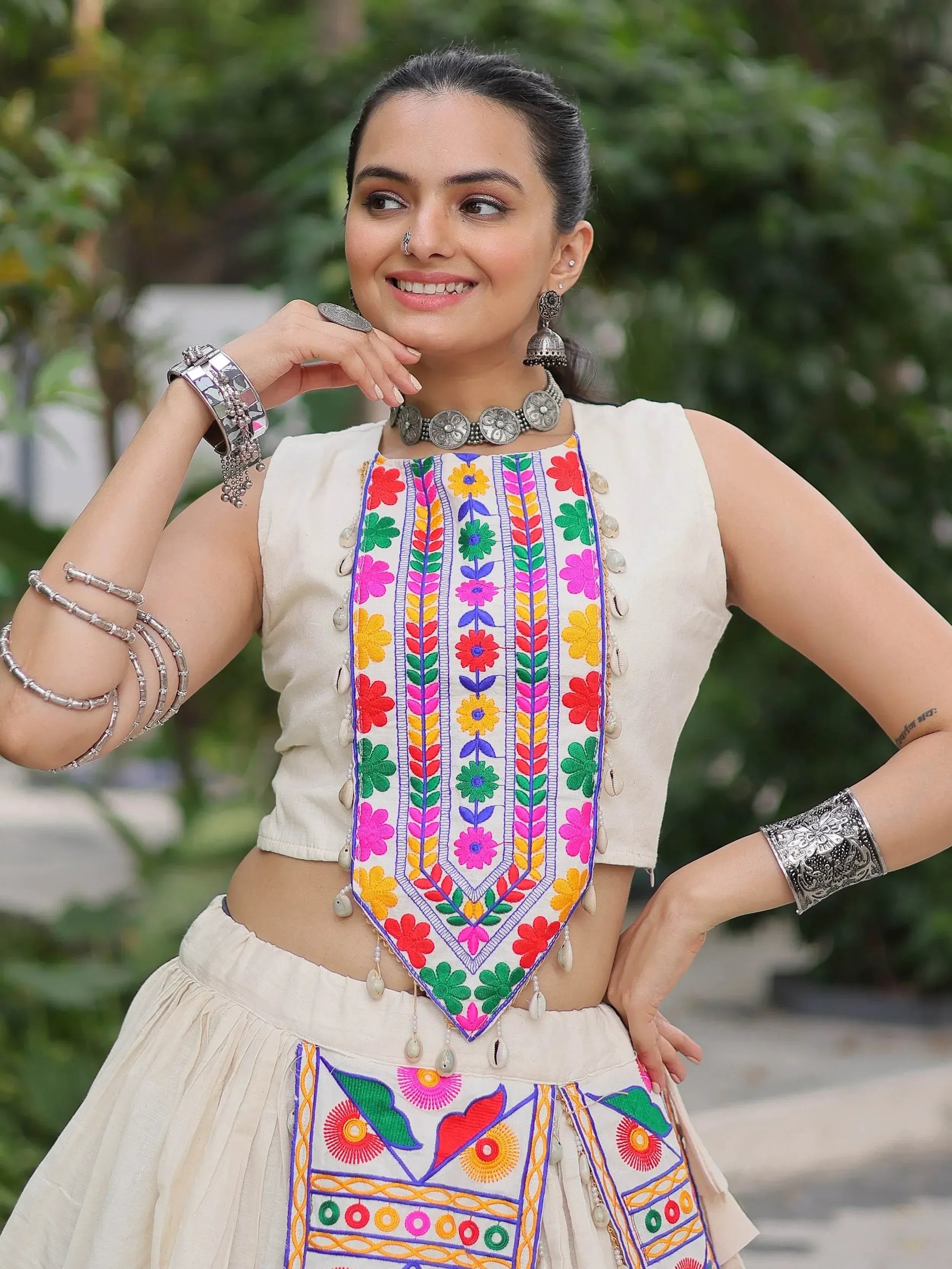 Woman in vibrant floral embroidered ethnic top and skirt with silver jewelry, perfect for Indian festive wear.