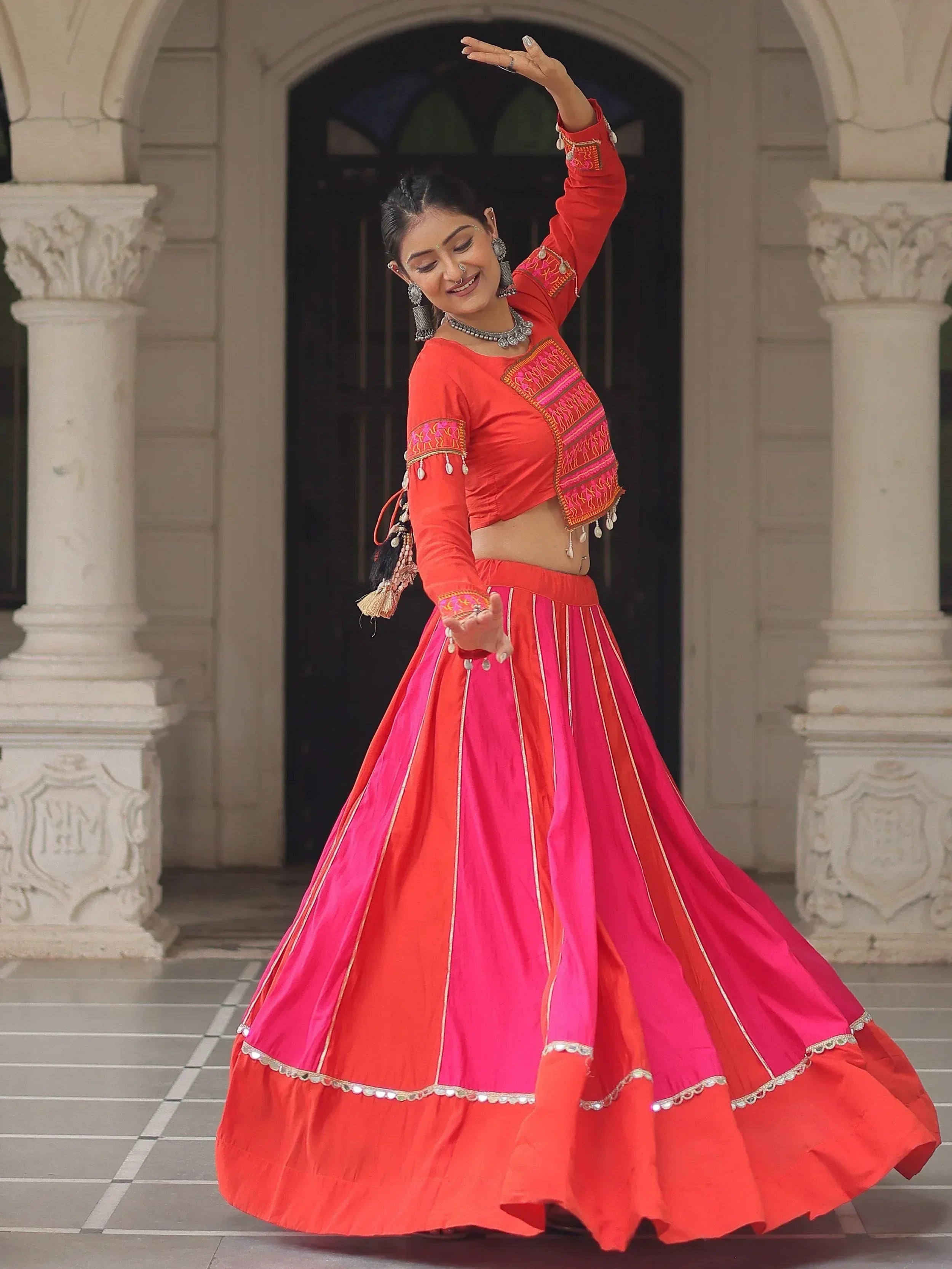Woman in vibrant red and pink lehenga choli with embroidery, dancing gracefully in traditional Indian attire