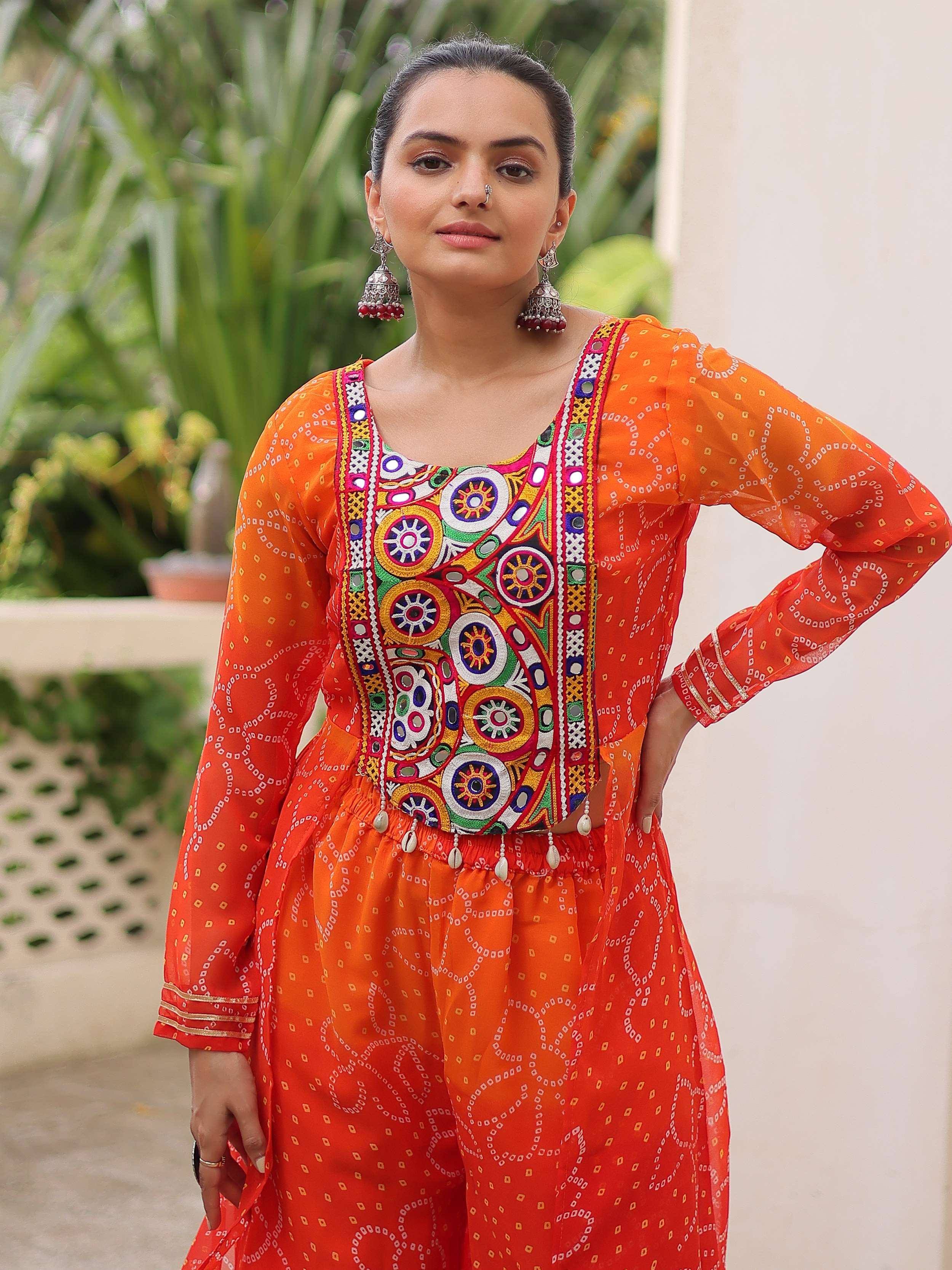 Vibrant orange ethnic wear with colorful mirror work and bandhani print, perfect for festive occasions.