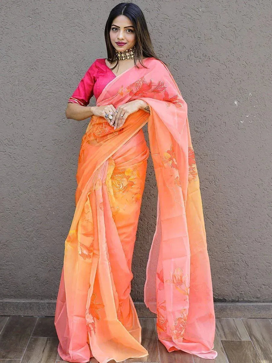 Woman in vibrant orange-pink floral saree with matching blouse, ethnic Indian wear