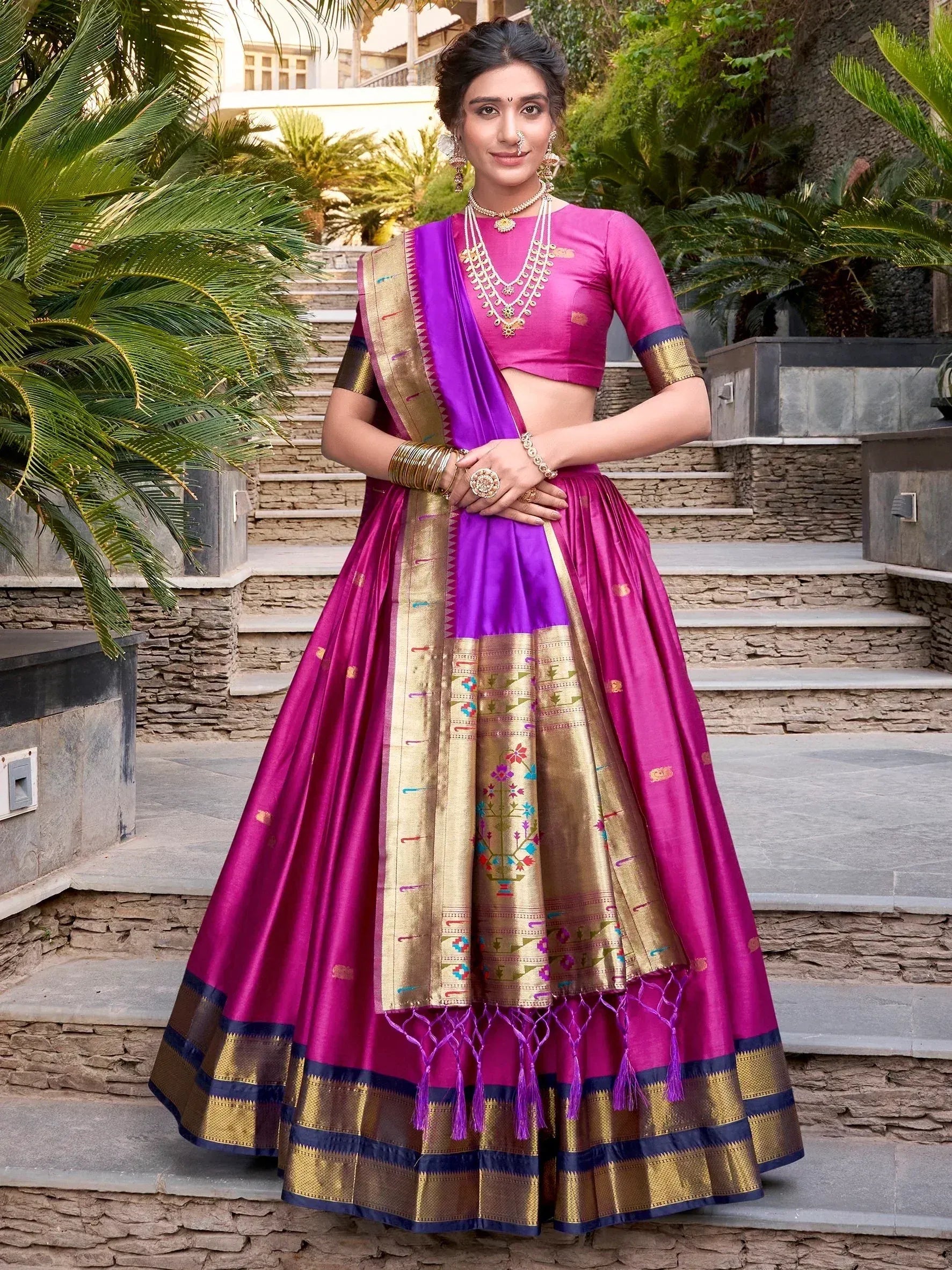 Woman in vibrant pink and purple designer lehenga choli with gold embroidery, perfect for Indian ethnic occasions.
