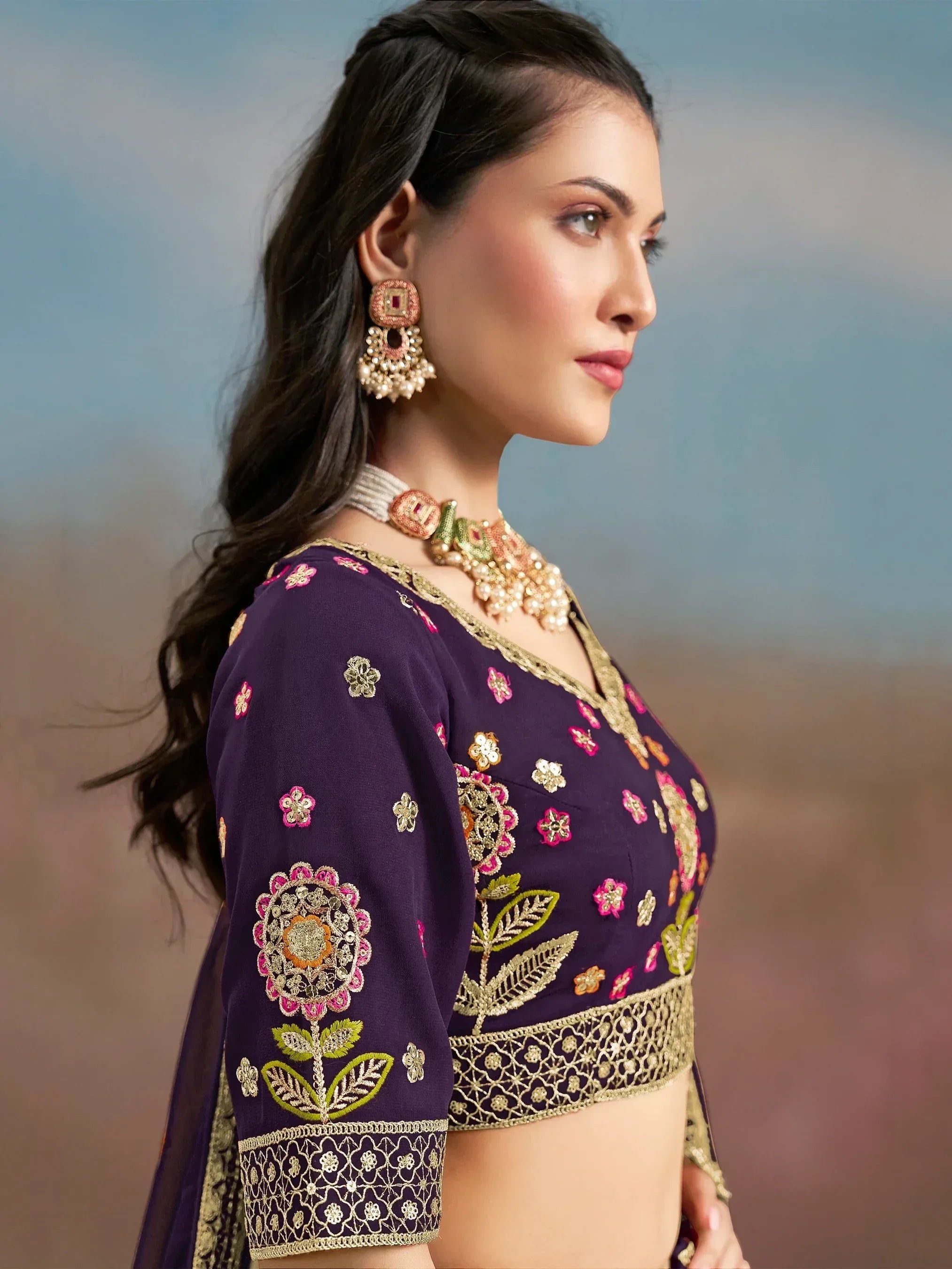 Purple embroidered designer blouse with floral motifs, gold trim, and matching ethnic jewelry for Indian wear.