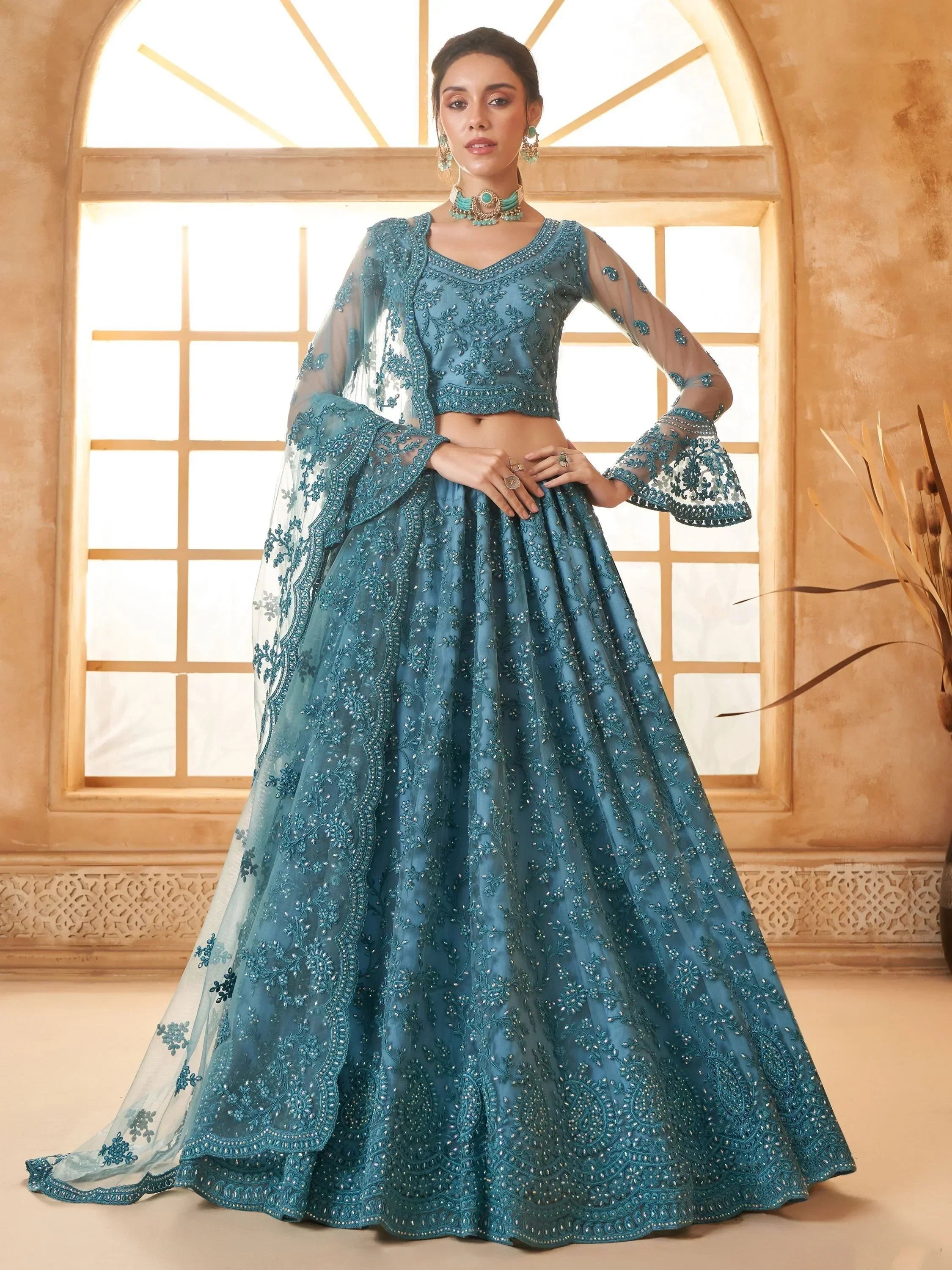 Teal blue embroidered lehenga choli with sheer bell sleeves, perfect for Indian weddings and festive occasions.