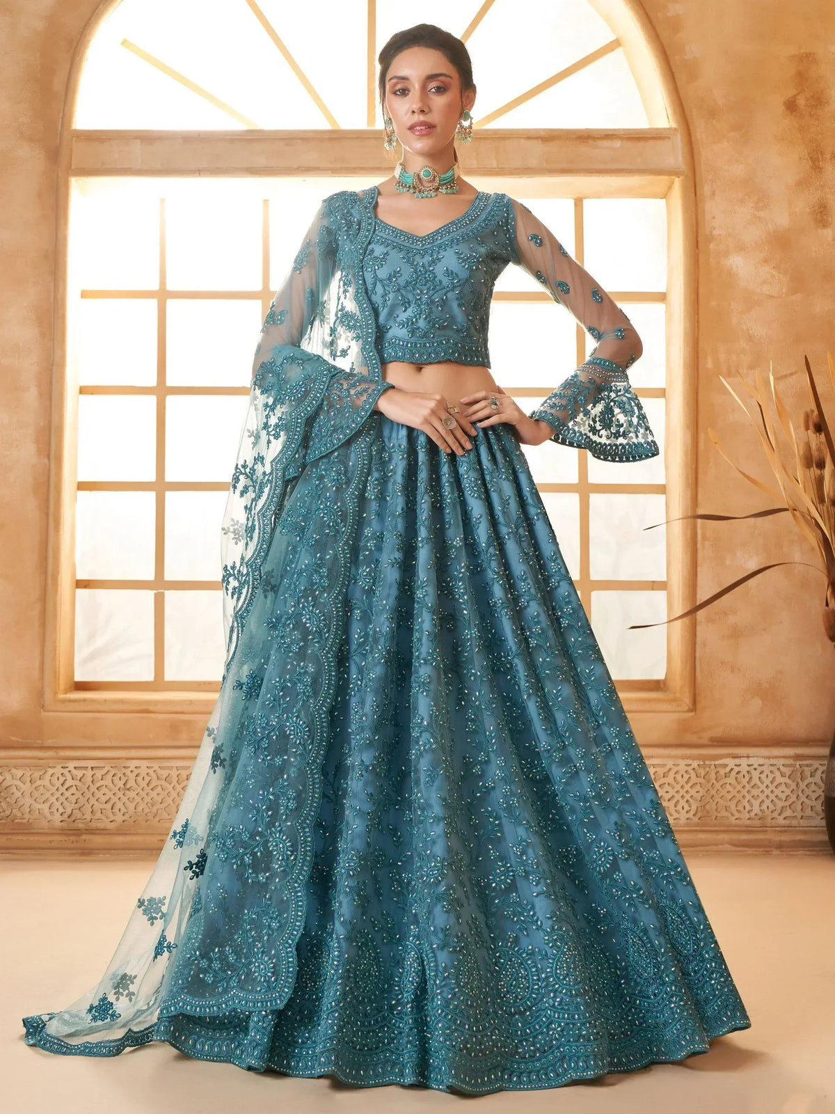 Teal blue embroidered lehenga choli with sheer bell sleeves, perfect for Indian weddings and festive occasions.