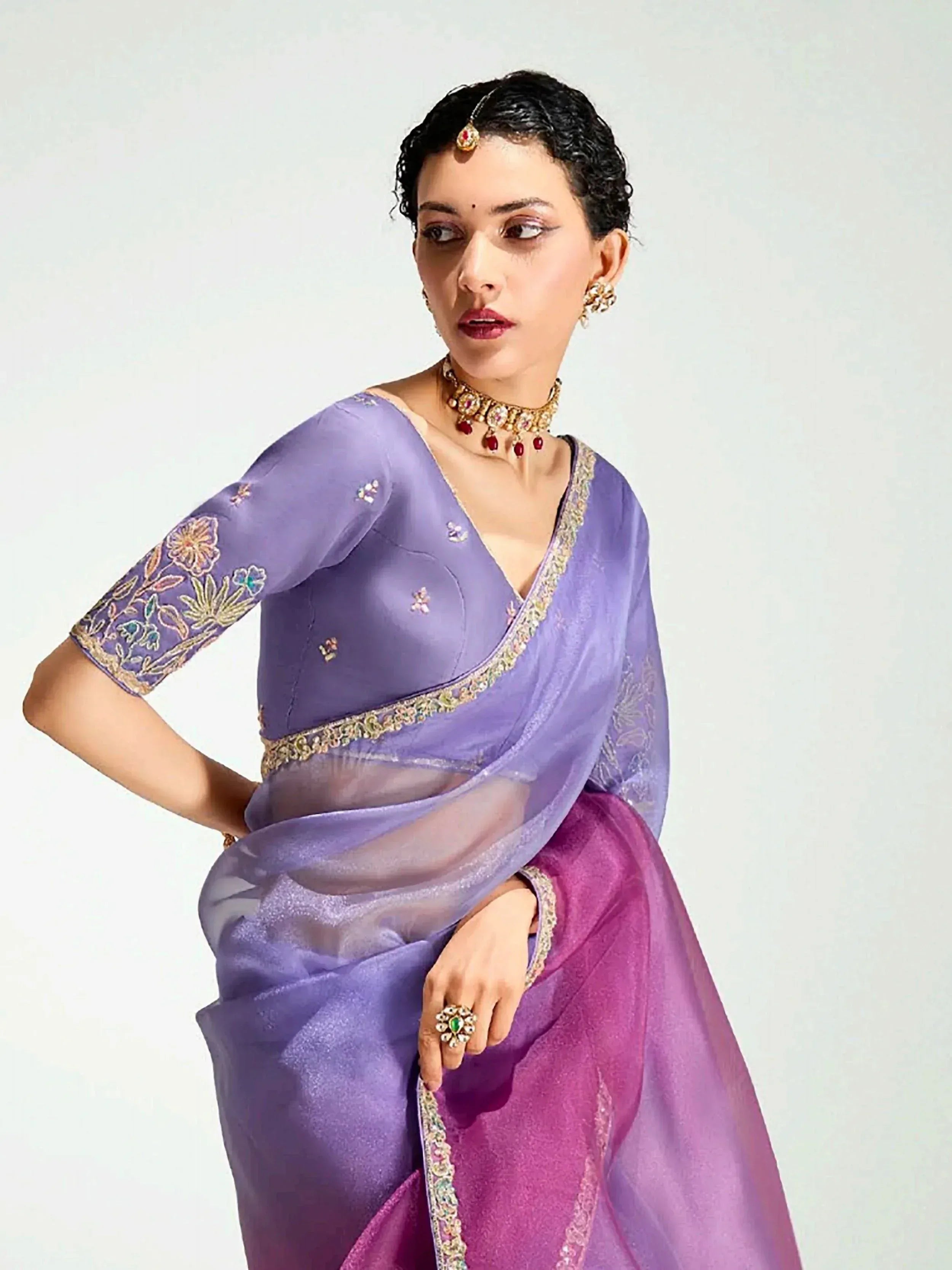 Purple embroidered saree with floral detailing and gold trim, paired with traditional Indian jewelry