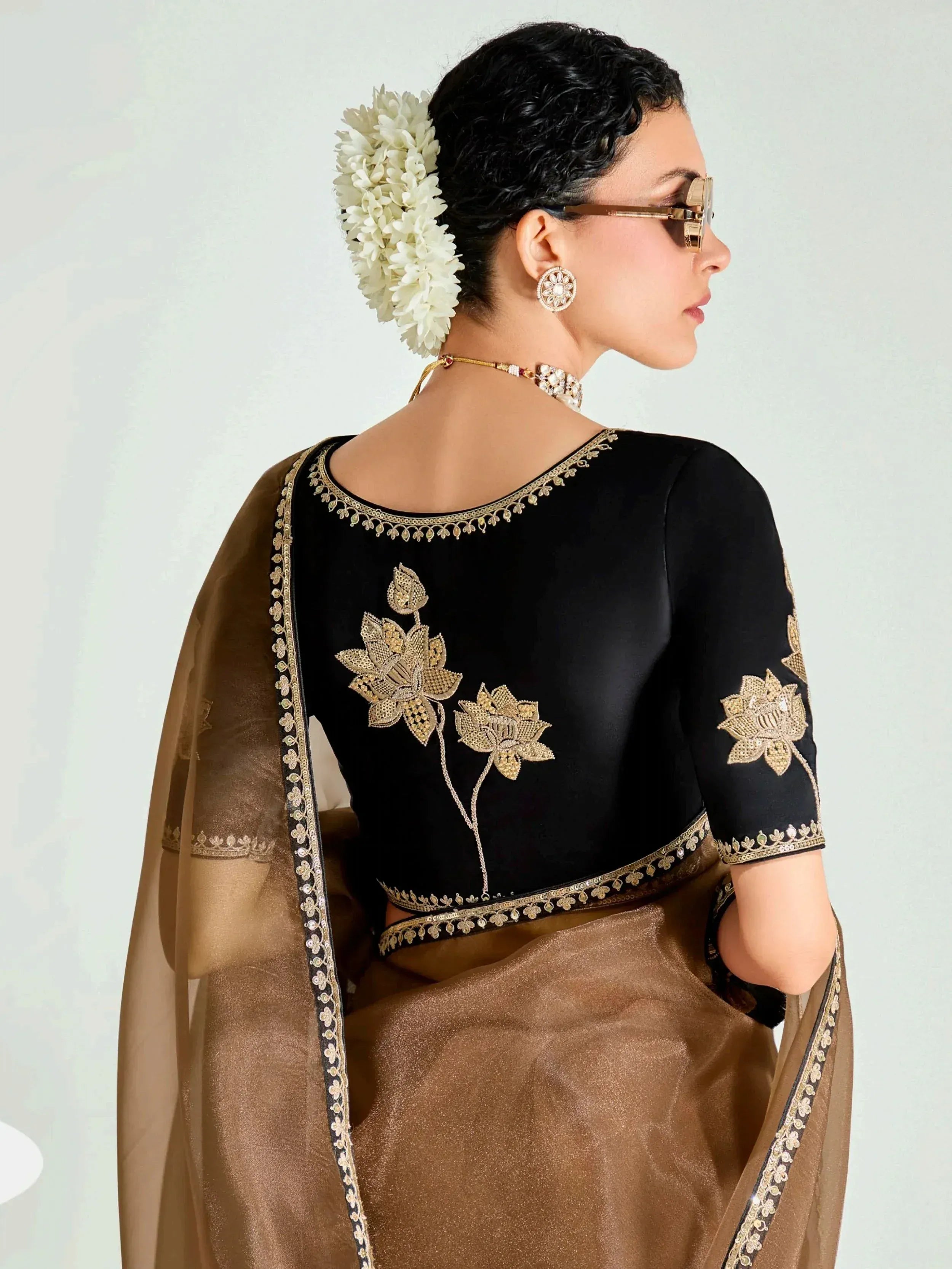 Black and gold embroidered ethnic saree blouse with floral design, paired with brown saree and white flowers in hair