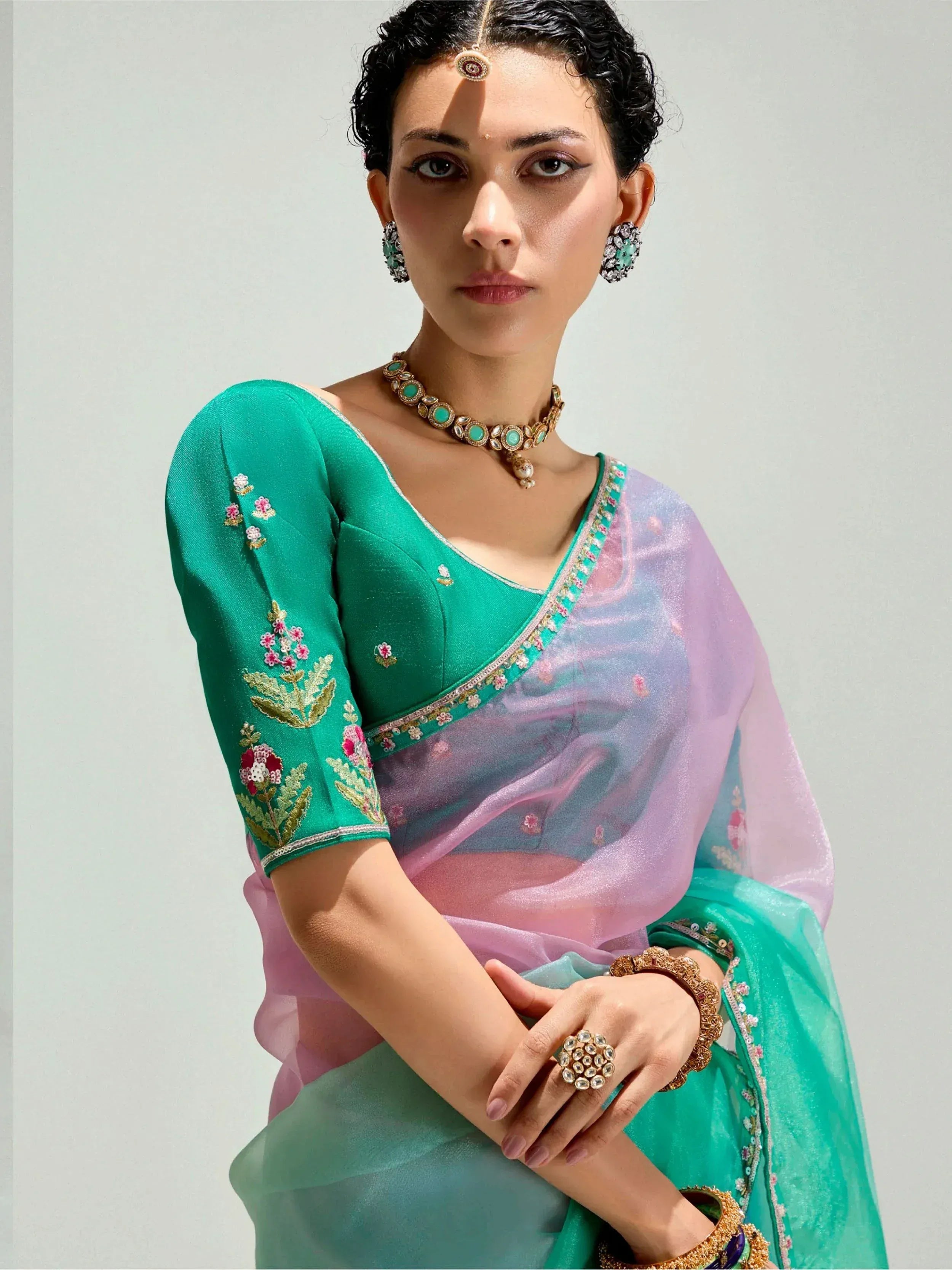 Woman in elegant green embroidered saree with floral details and traditional jewelry, showcasing Indian ethnic wear.