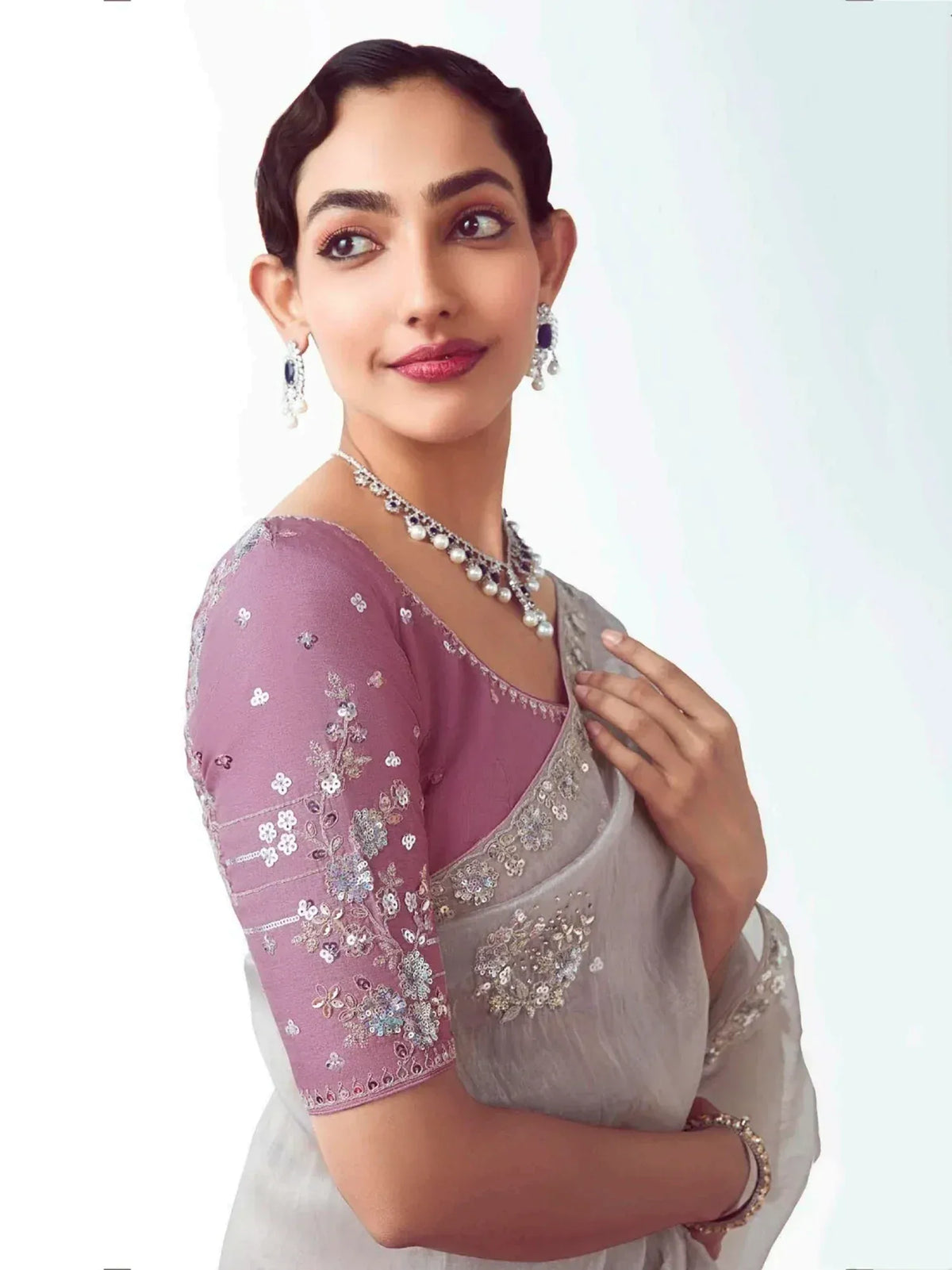 Woman in elegant grey saree with pink embroidered blouse, pearl necklace, and statement earrings