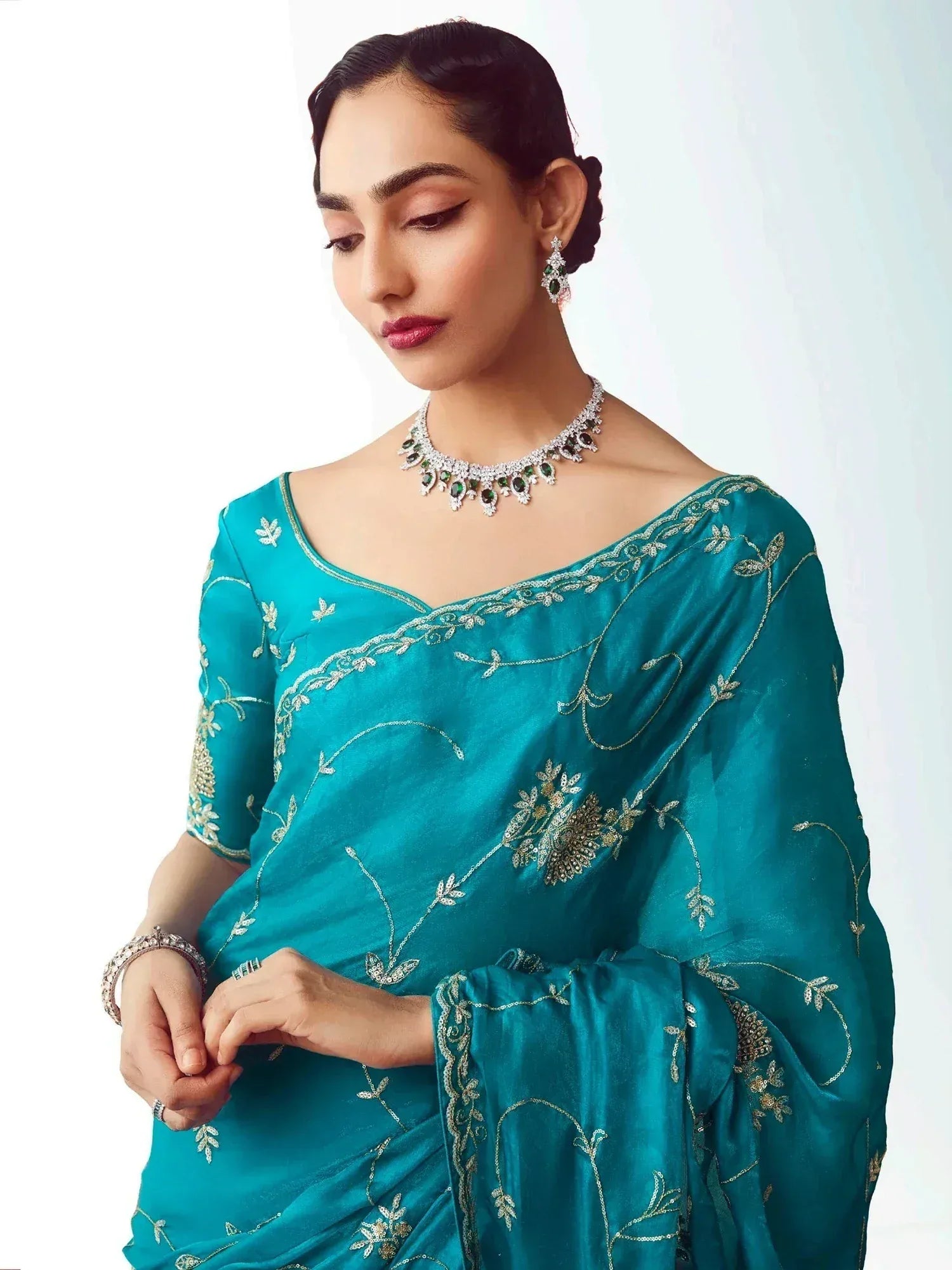 Teal embroidered saree with gold threadwork, paired with emerald and diamond jewelry for ethnic wear