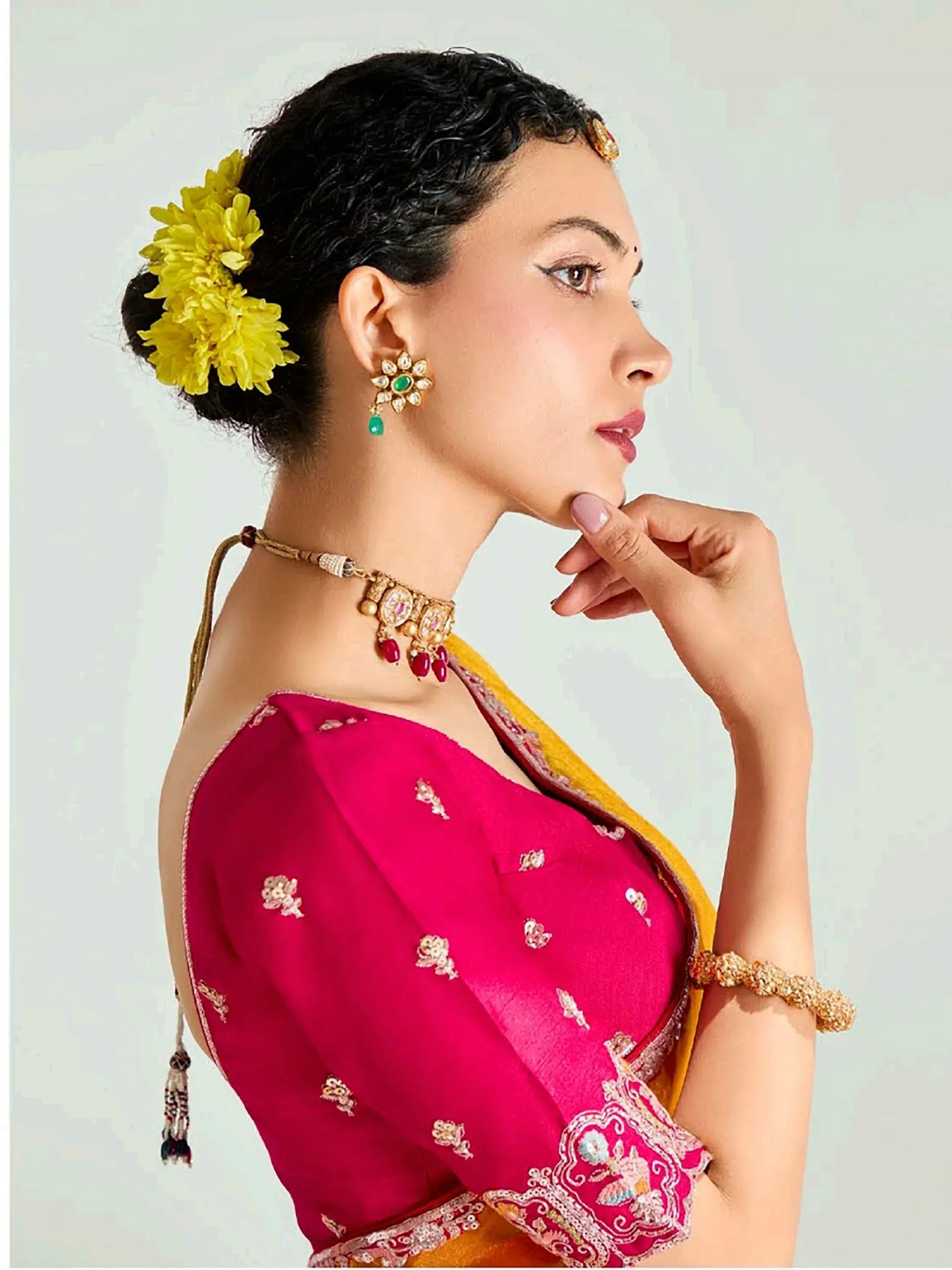 Woman in pink embroidered blouse with yellow saree, traditional Indian jewelry and floral hair accessory
