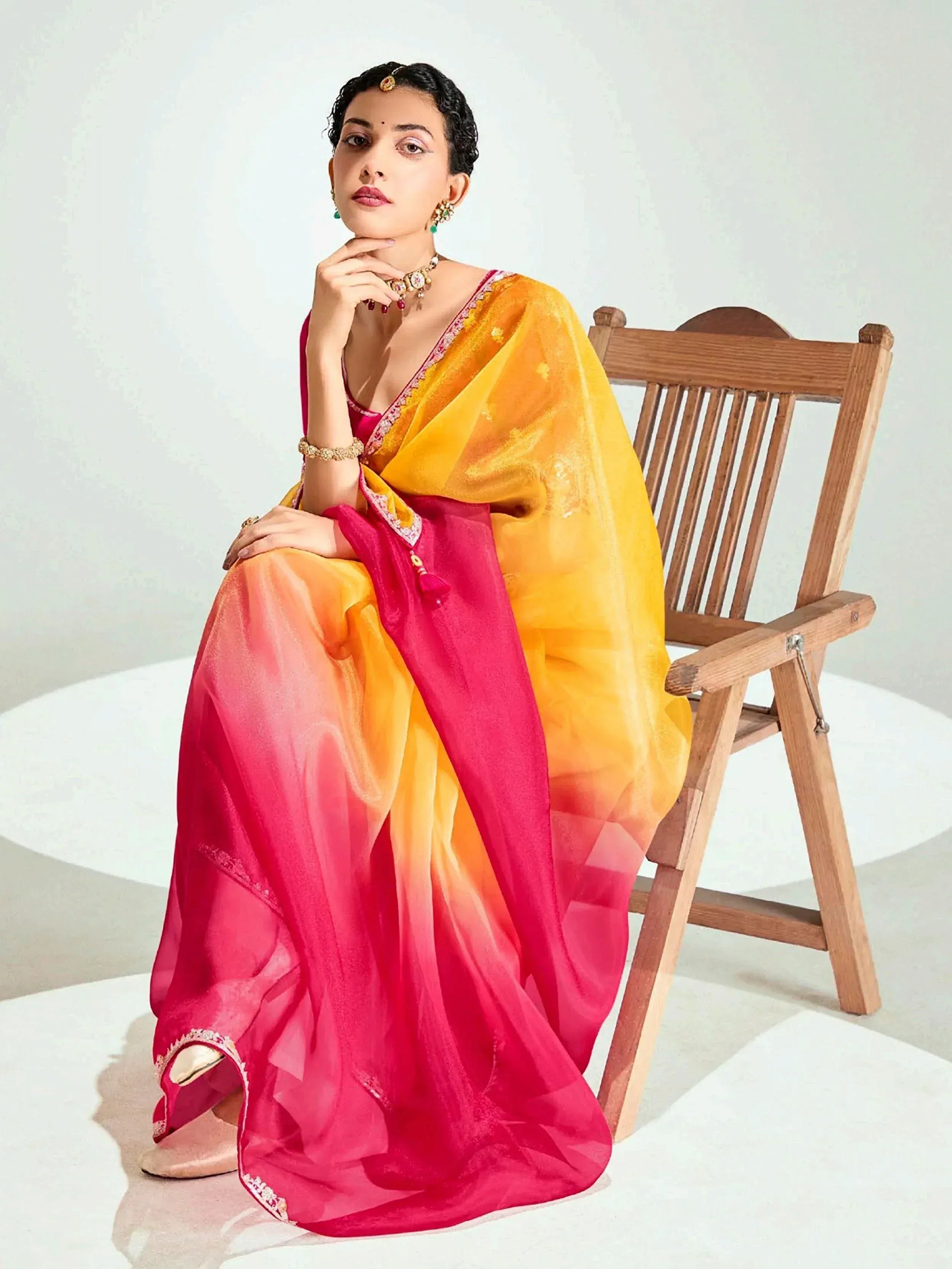 Woman in vibrant pink and yellow ombre saree with embroidery, styled with traditional jewelry for ethnic wear.