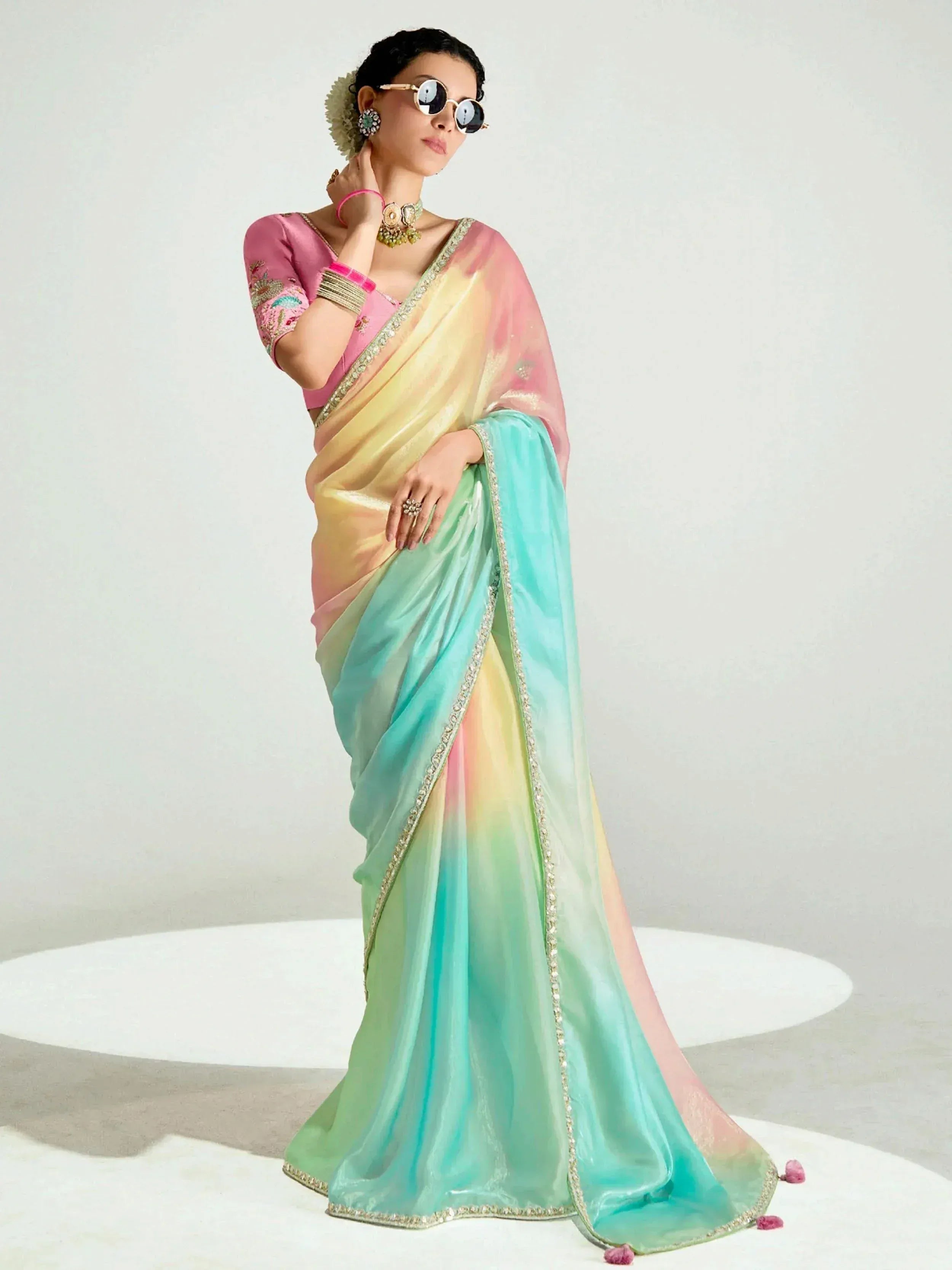 Woman in colorful ombre saree with pink blouse, ethnic jewelry, and sunglasses, showcasing designer Indian ethnic wear.