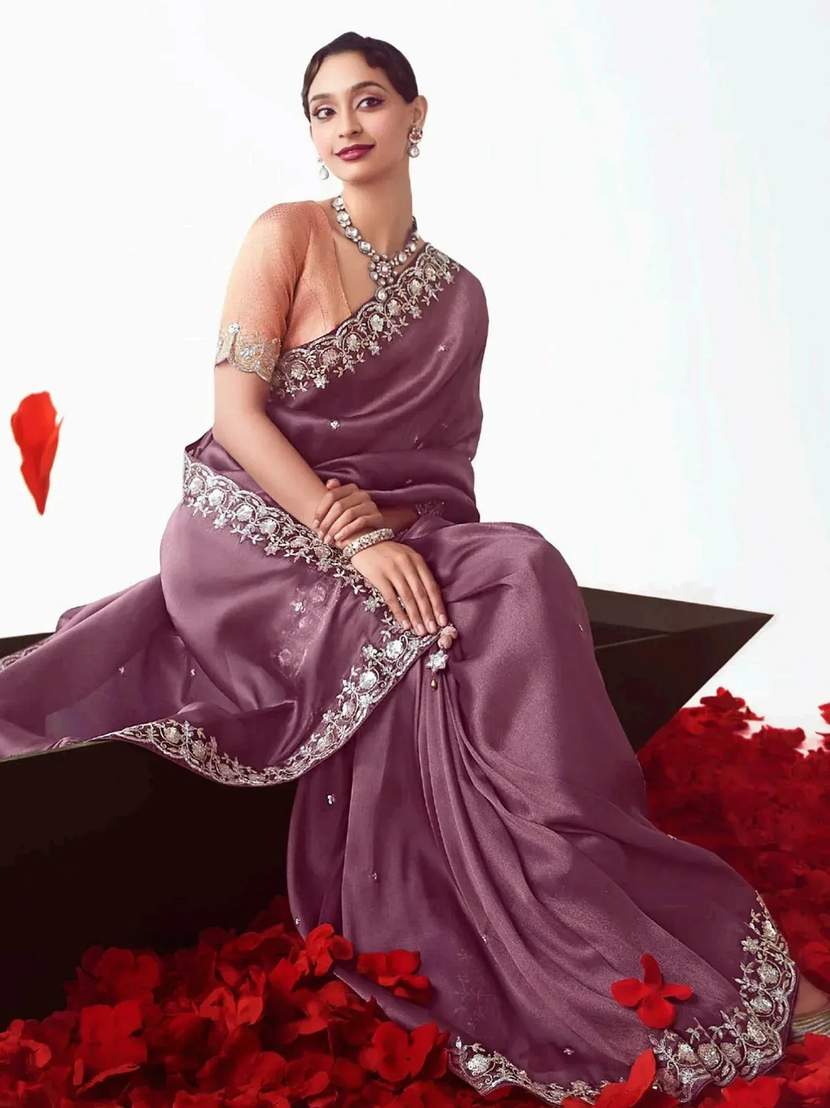 Elegant purple saree with heavy silver embroidery, paired with matching blouse and jewelry, styled with red rose petals.