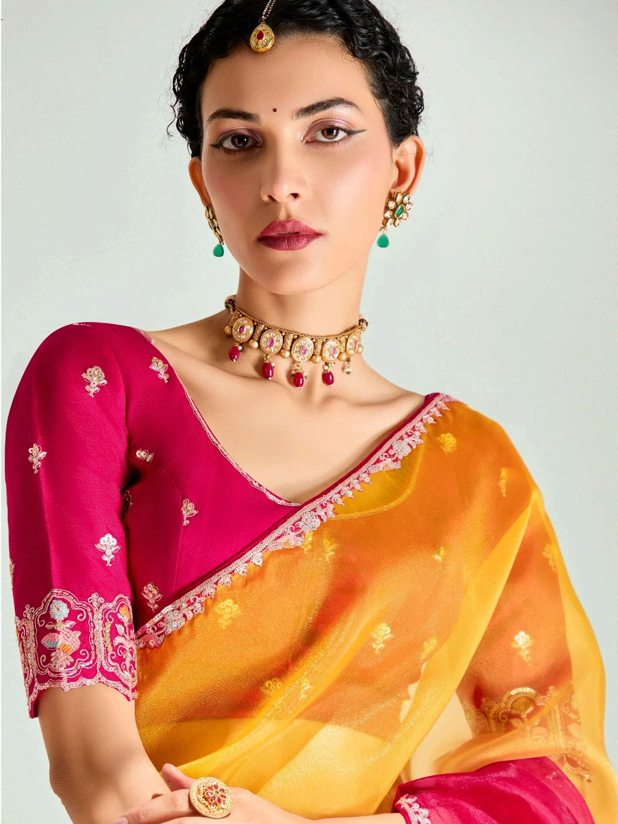 Woman in vibrant pink and orange saree with embroidery, traditional Indian jewelry, and maang tikka