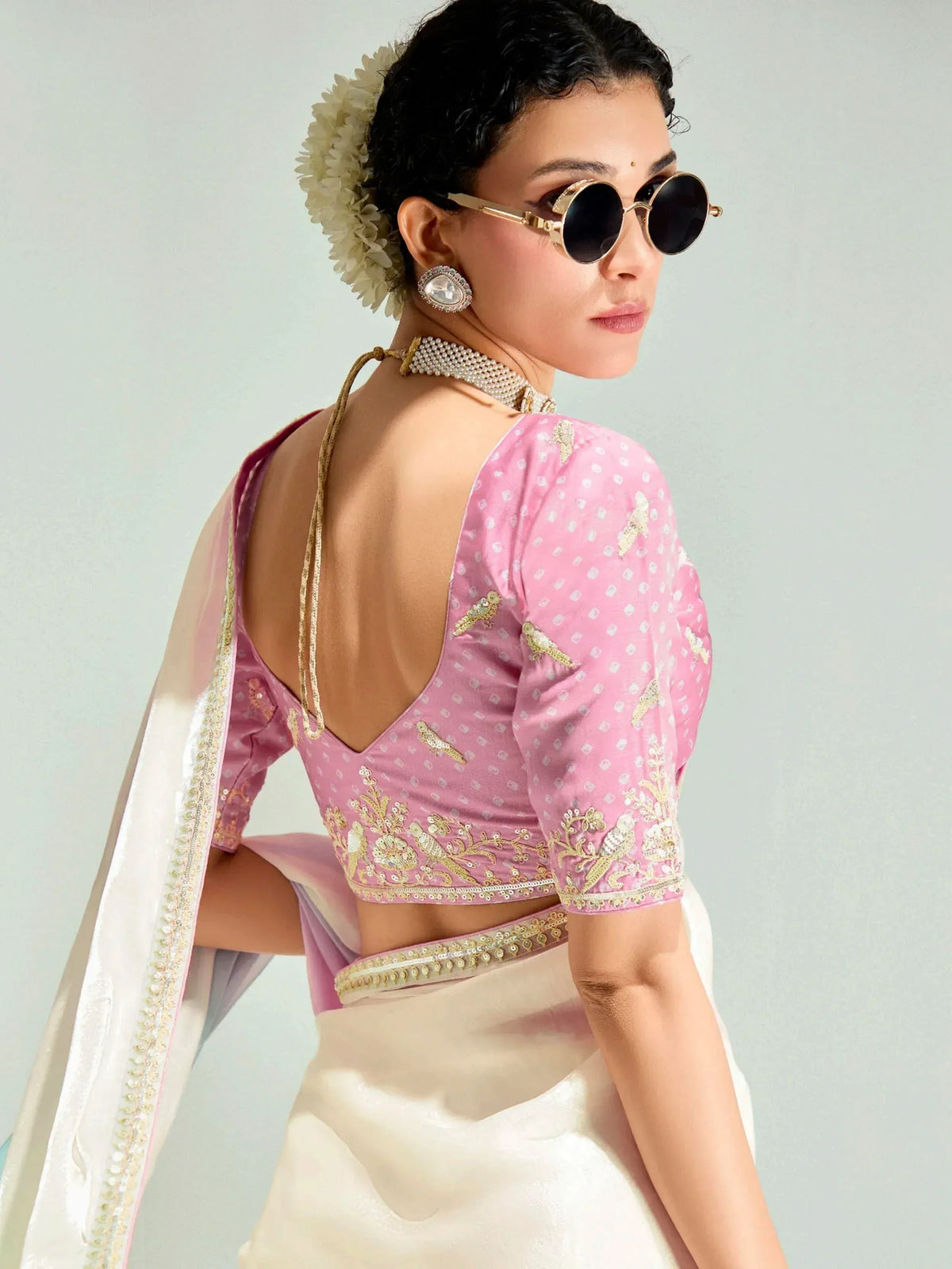 Pink embroidered blouse with backless design, paired with white saree and floral hair accessory