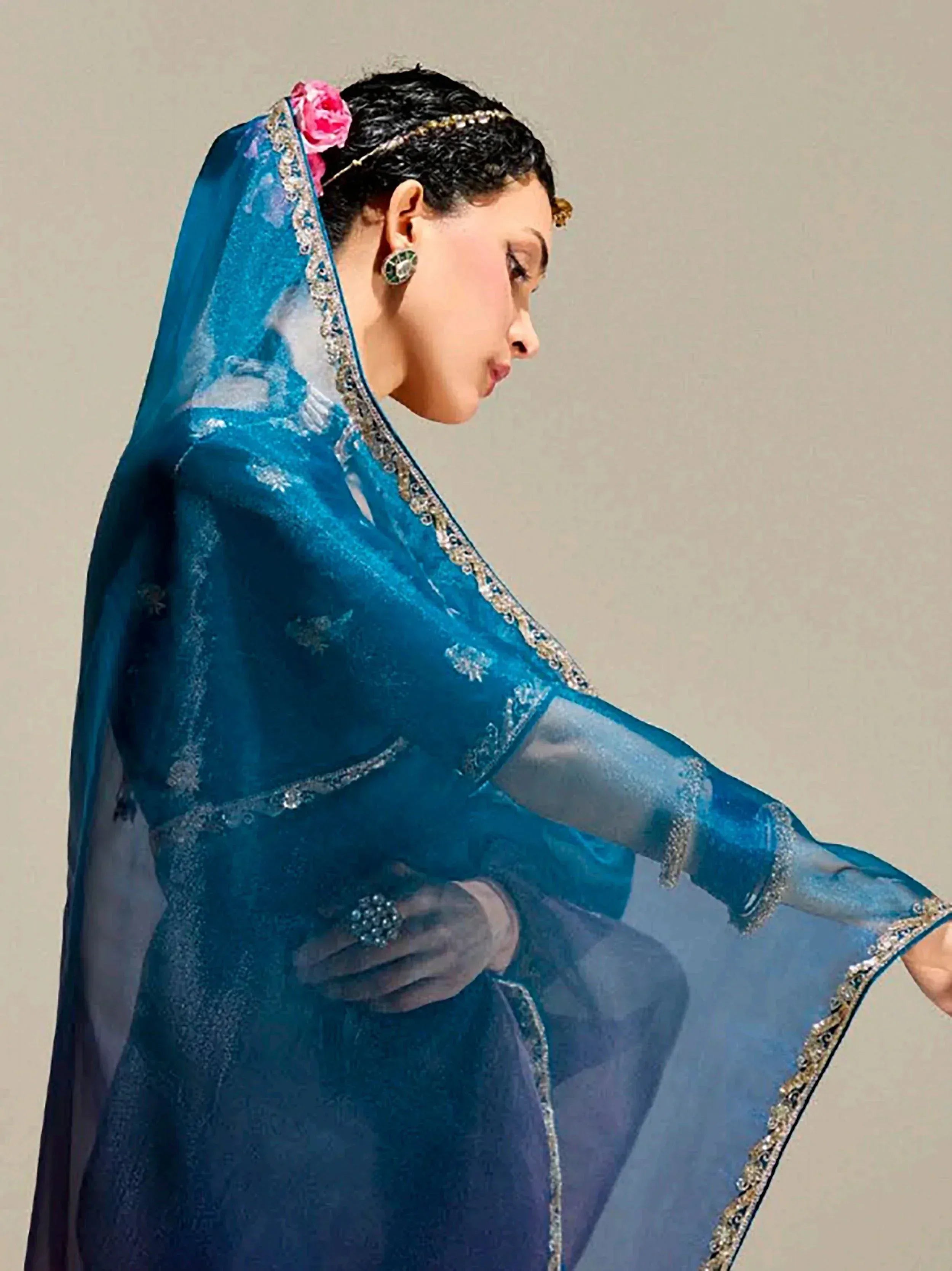 Woman in elegant blue Indian ethnic gown with sheer dupatta, floral hair accessory, and traditional jewelry