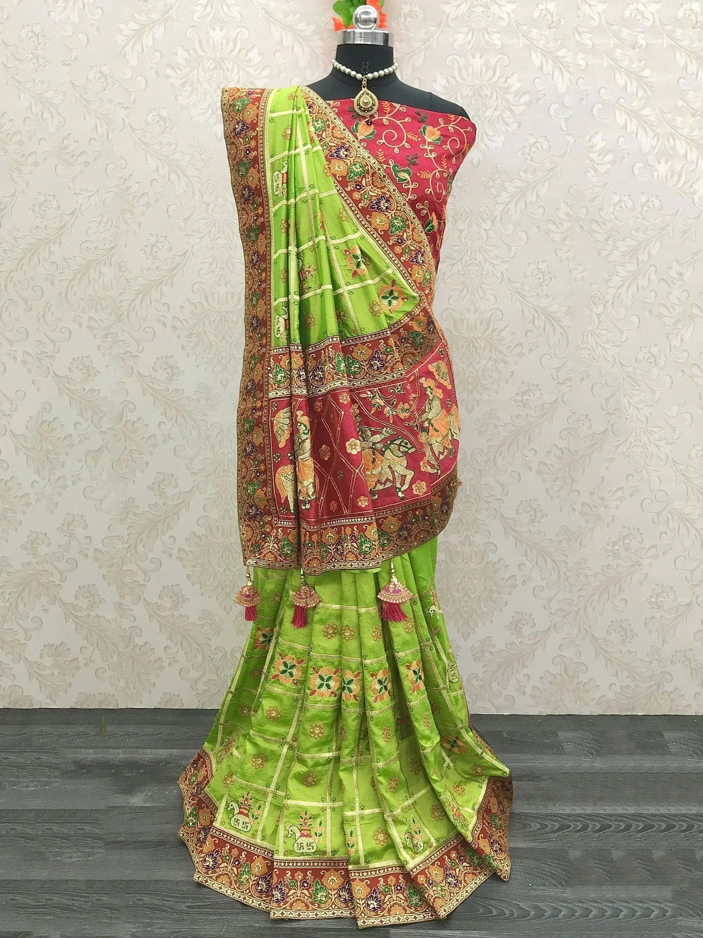 Green and red embroidered saree with floral and elephant motifs, displayed on mannequin with pearl necklace