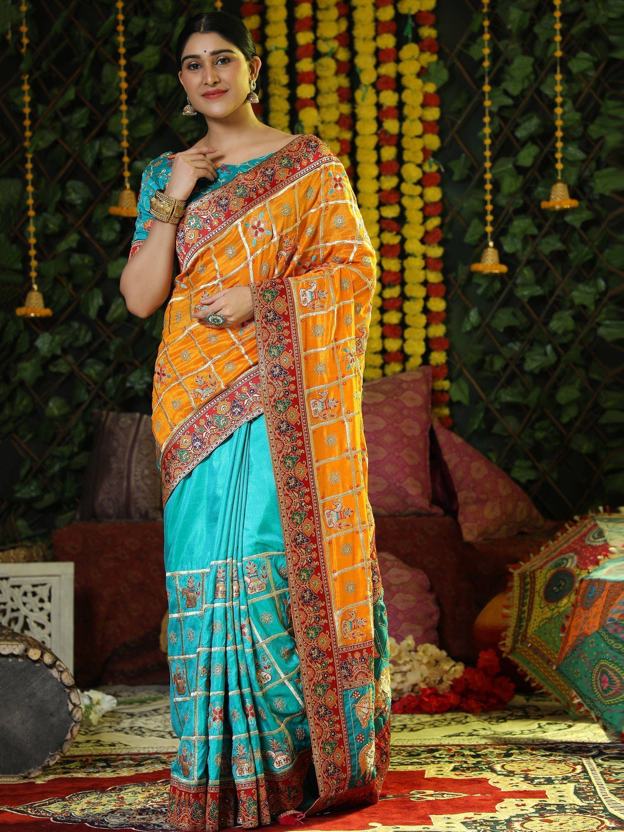Woman in vibrant orange and turquoise embroidered saree with floral and elephant motifs, perfect for Indian ethnic occasions.