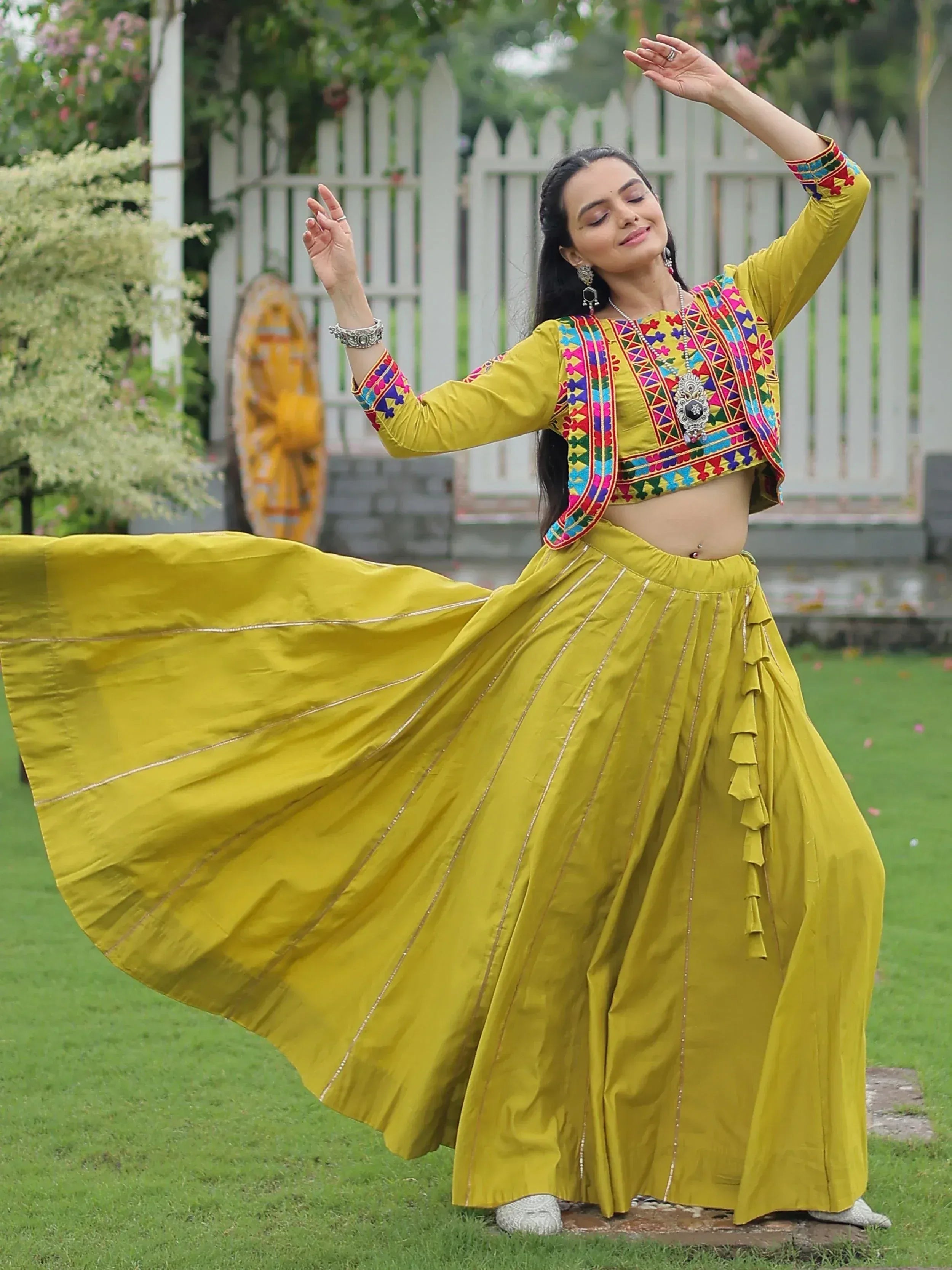 Woman in vibrant yellow embroidered lehenga choli dancing outdoors, Indian ethnic wear