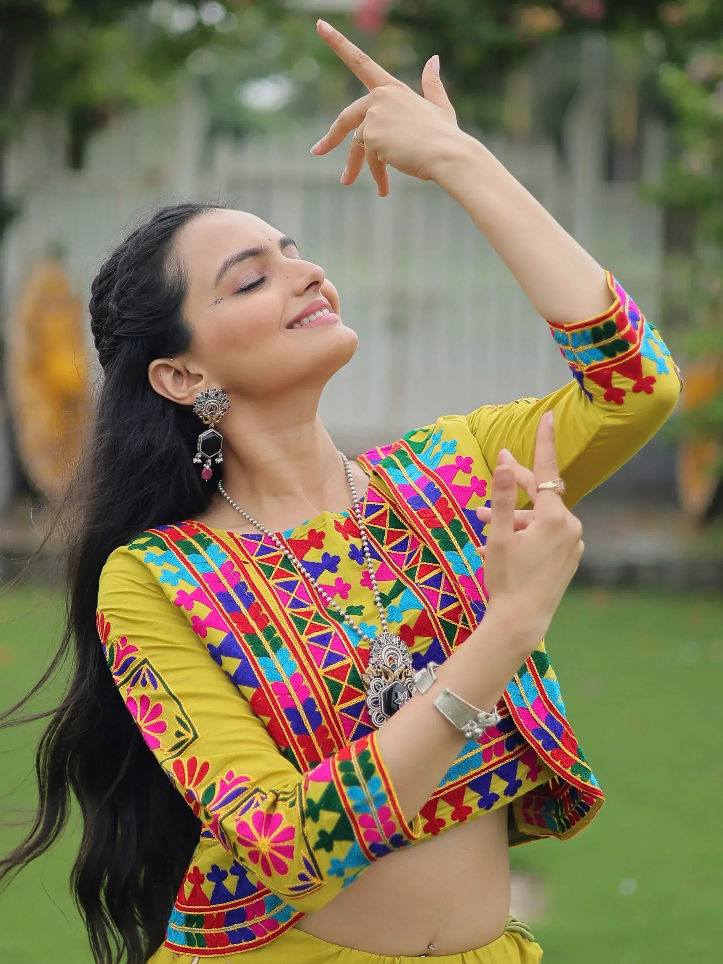 Woman in vibrant yellow embroidered ethnic top with colorful mirror work, traditional jewelry, dancing outdoors