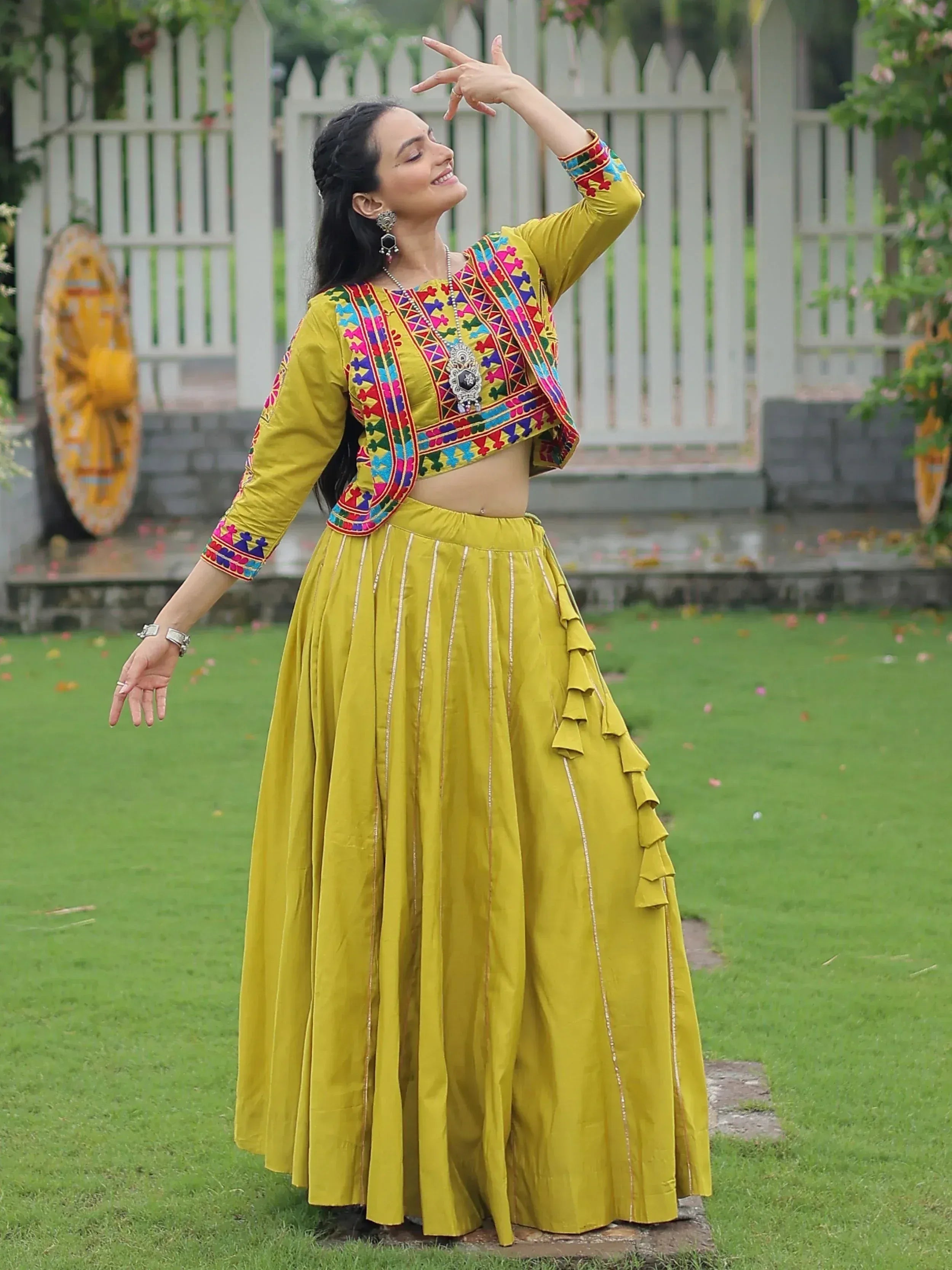 Woman in vibrant yellow ethnic lehenga choli with colorful embroidery, dancing outdoors