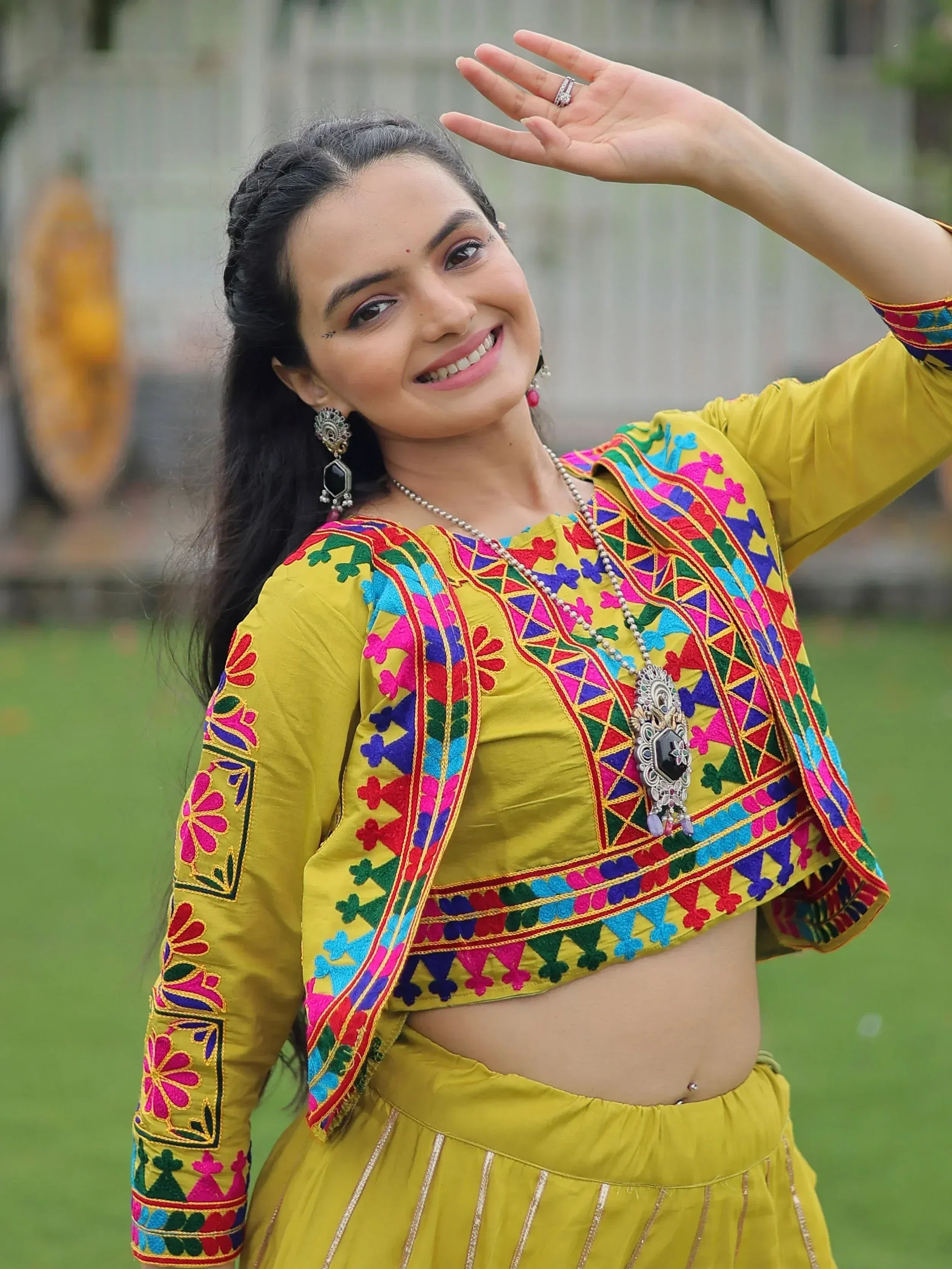 Woman in vibrant yellow embroidered Indian ethnic wear with colorful mirror work, perfect for festive occasions.