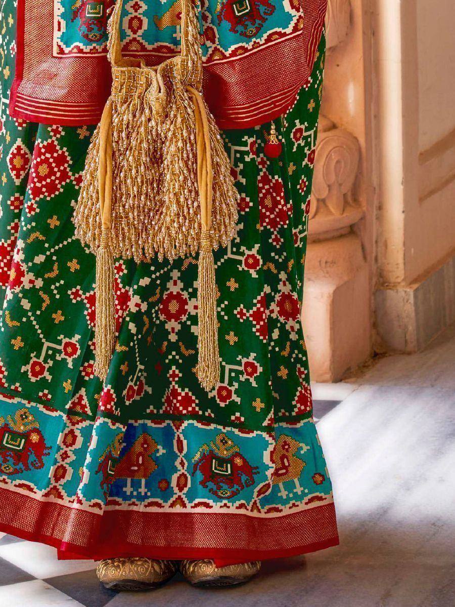 Vibrant green and red ethnic lehenga with elephant print, gold tassel bag, and traditional footwear