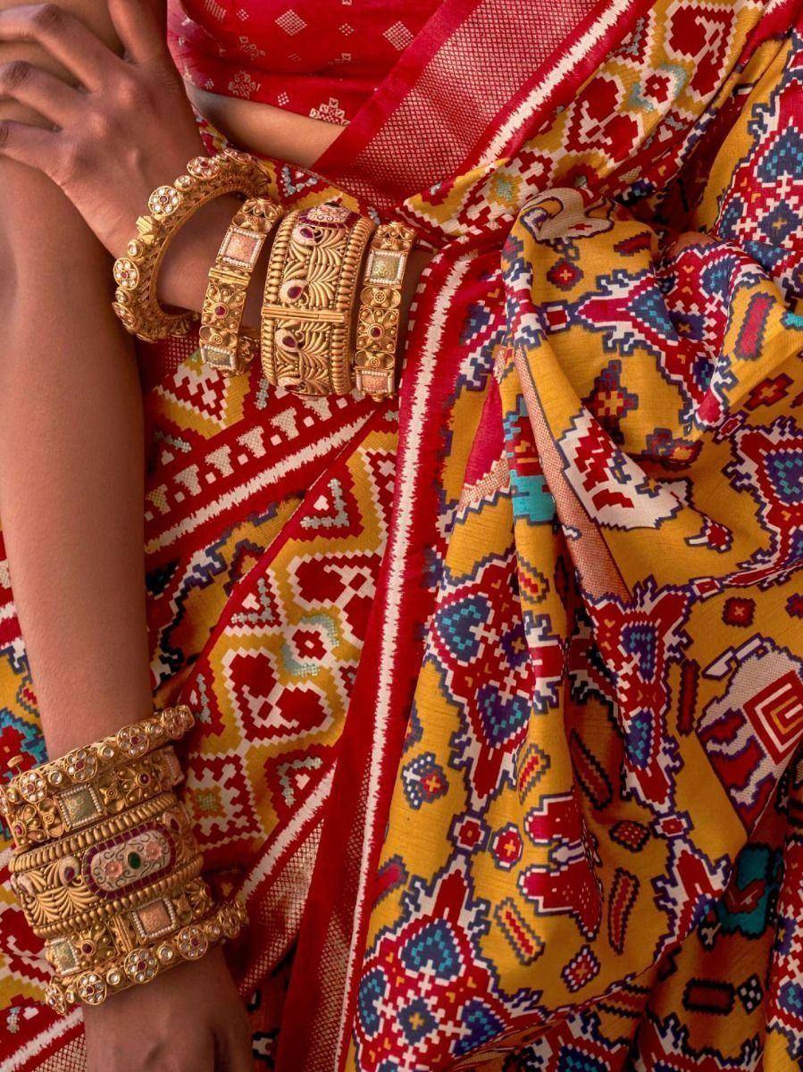 Vibrant red and yellow ethnic saree with intricate geometric patterns and traditional gold bangles