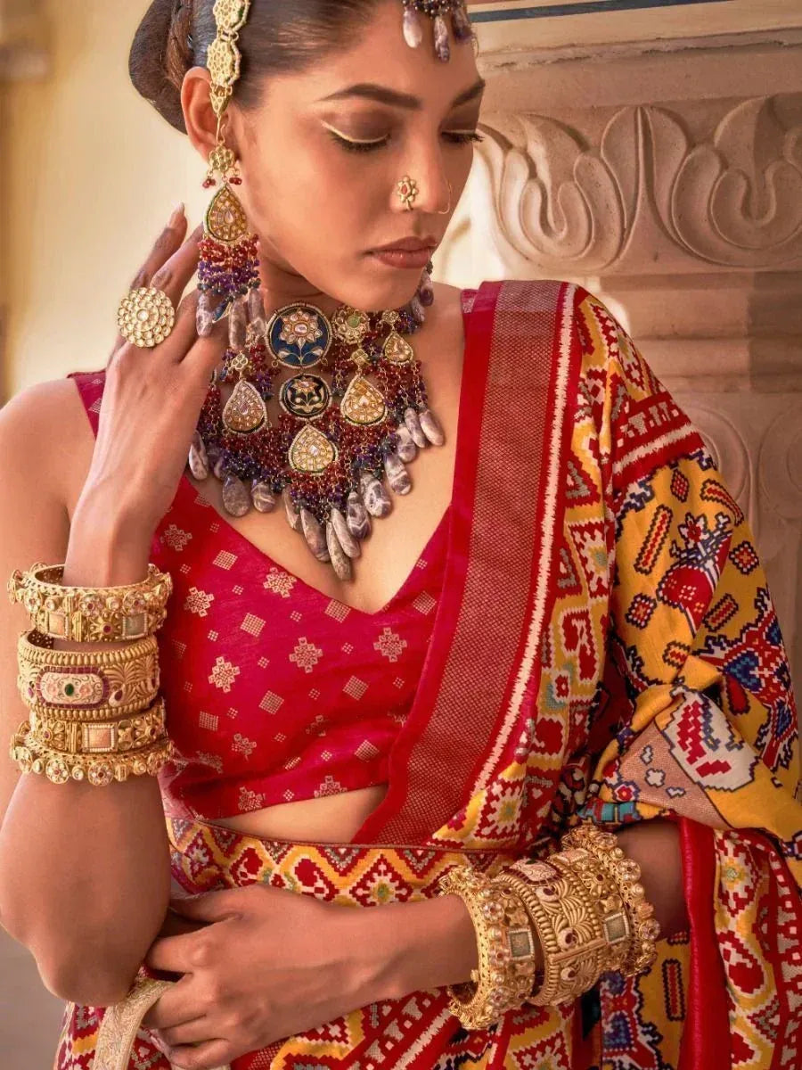 Woman in vibrant red and yellow ethnic saree with intricate jewelry and traditional Indian accessories