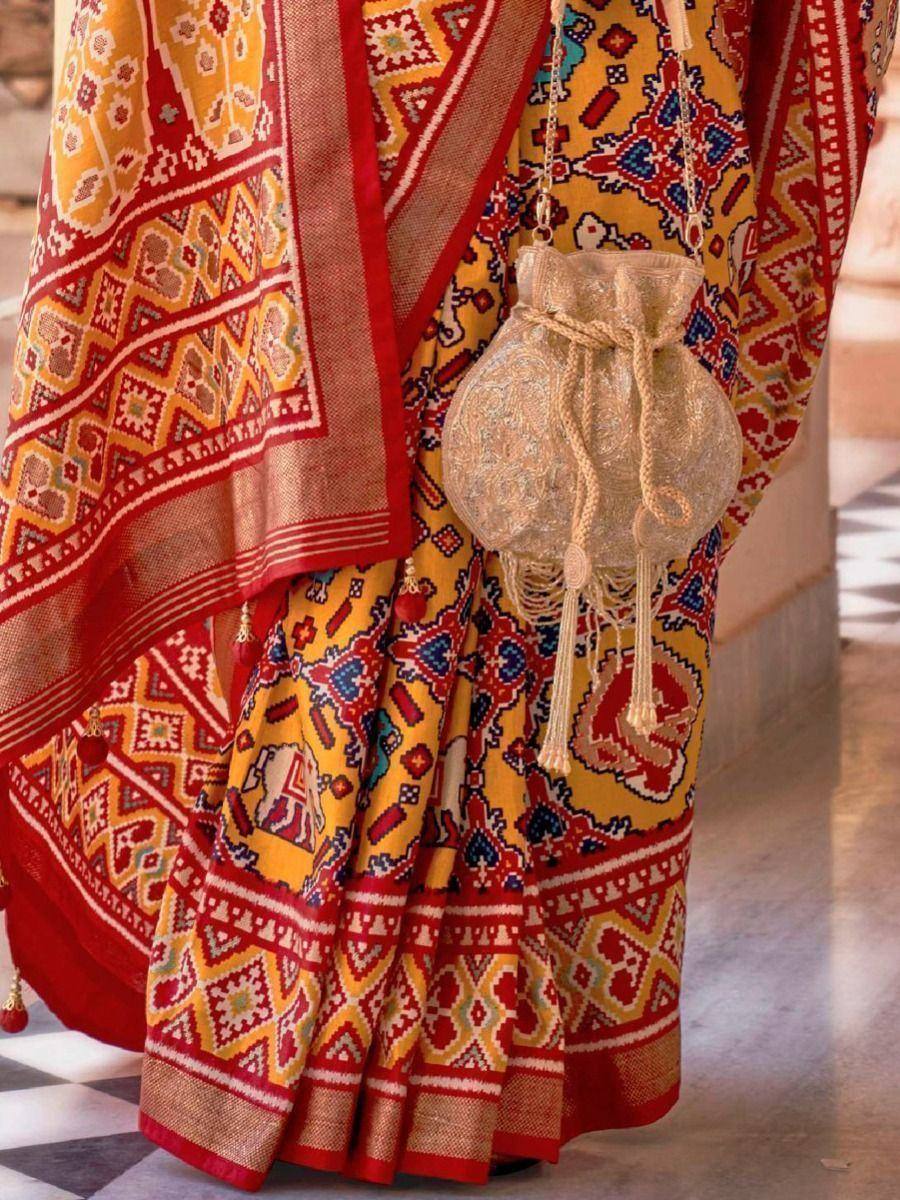 Vibrant yellow and red ethnic saree with intricate geometric patterns and matching potli bag, perfect for Indian festivities.