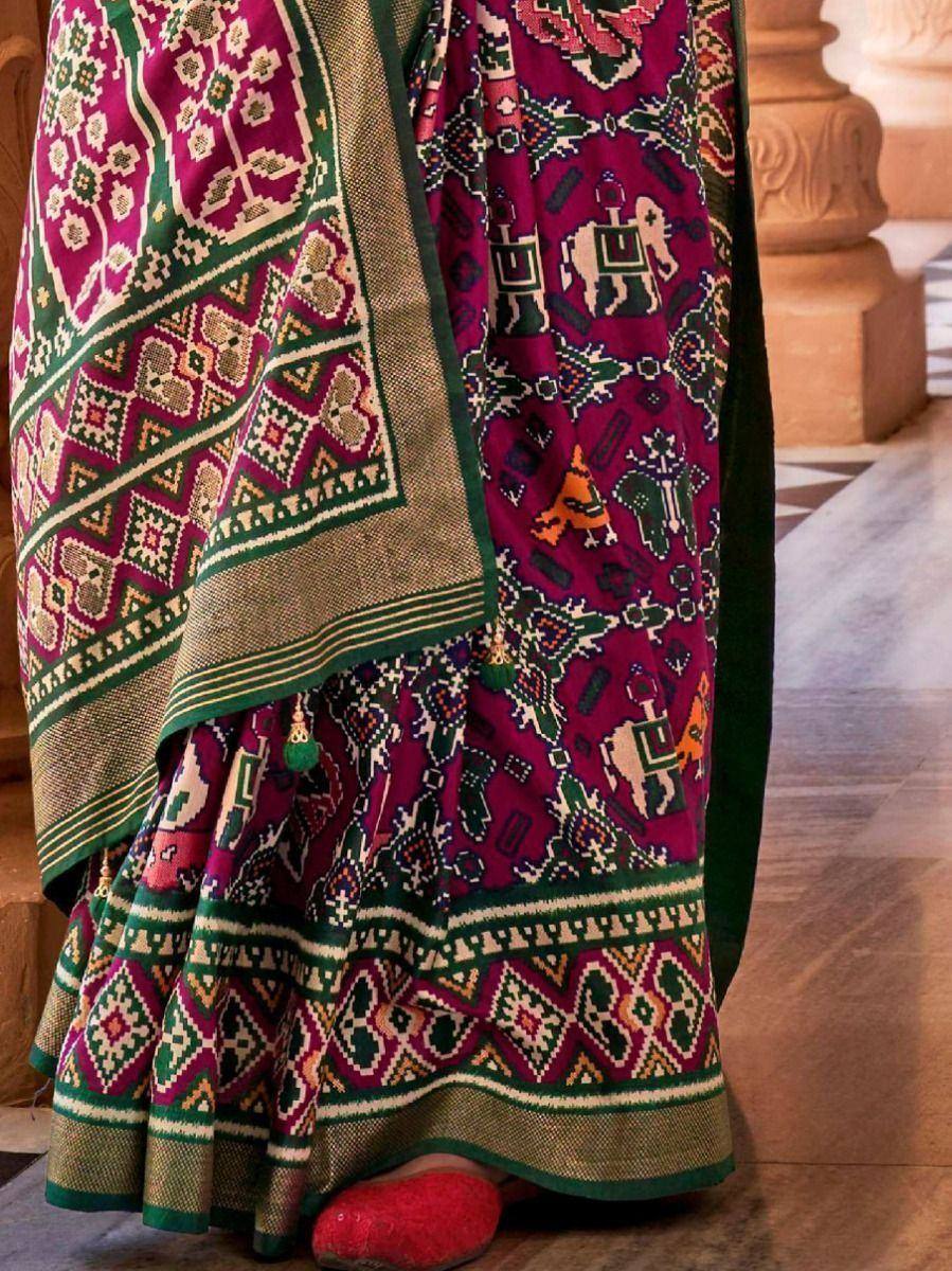 Vibrant purple and green ethnic saree with elephant motifs and geometric borders, paired with red footwear.