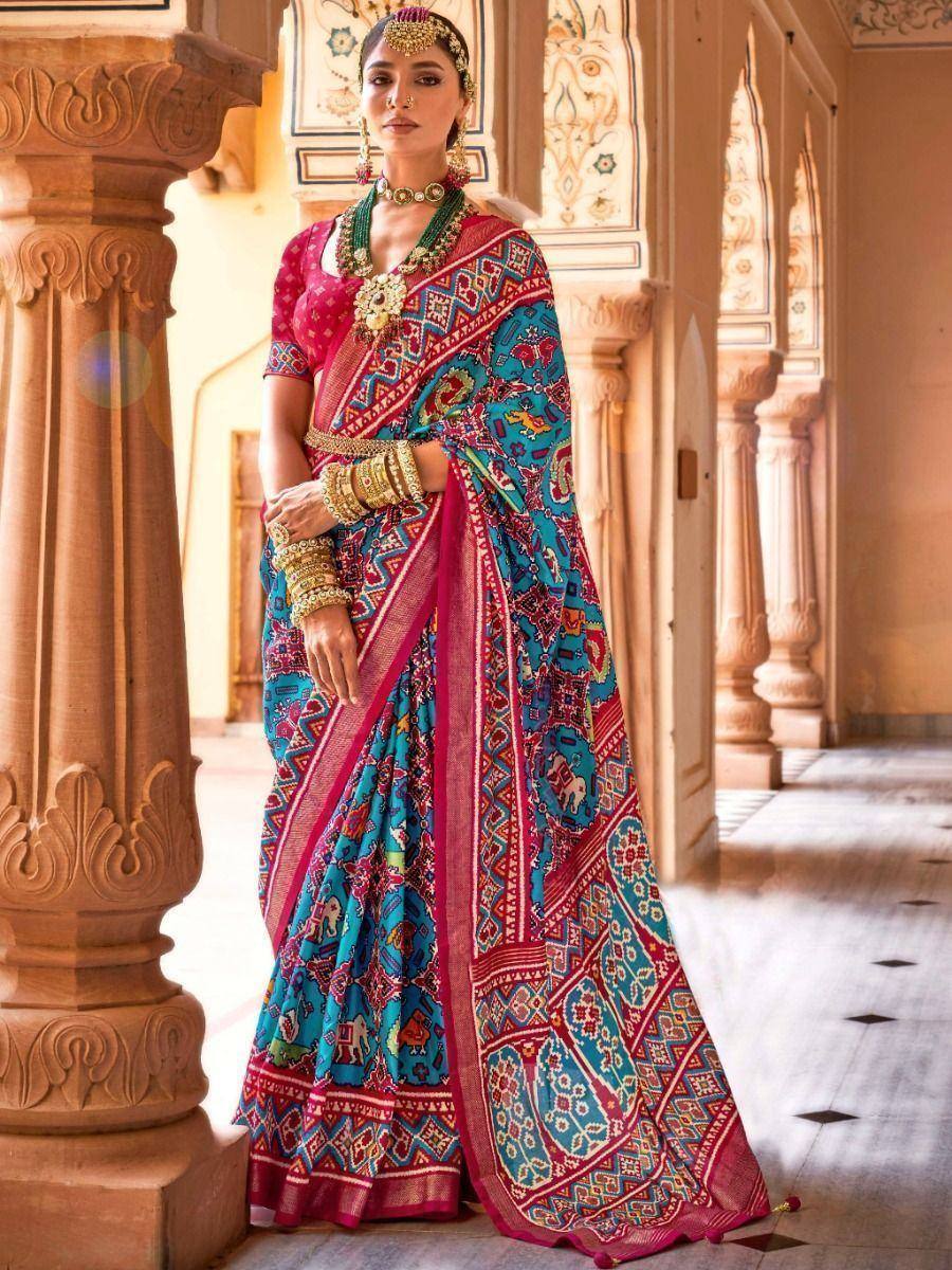 Vibrant blue and pink printed saree with elephant motifs, paired with gold jewelry, styled for Indian ethnic wear.