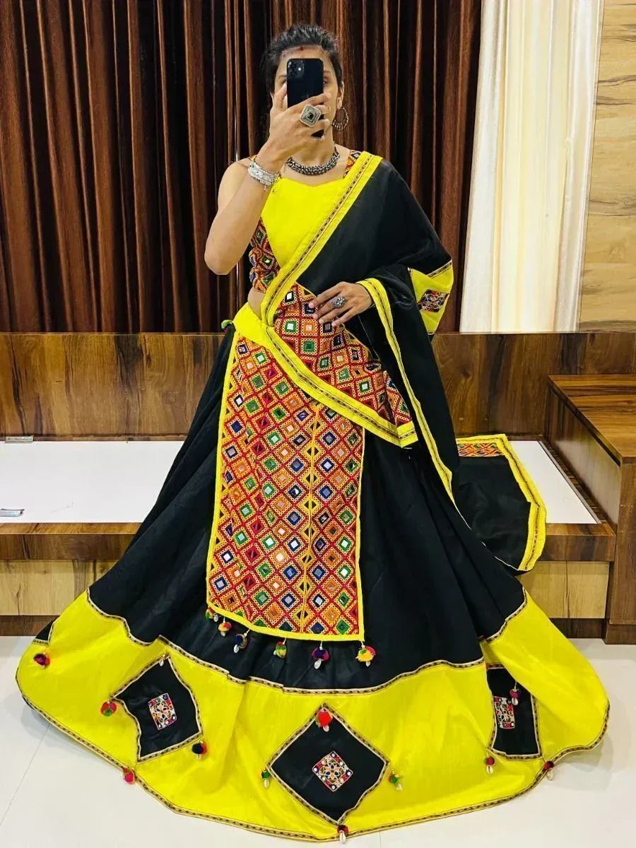 Black and yellow ethnic lehenga choli with colorful mirror work and pom poms, perfect for festive occasions.