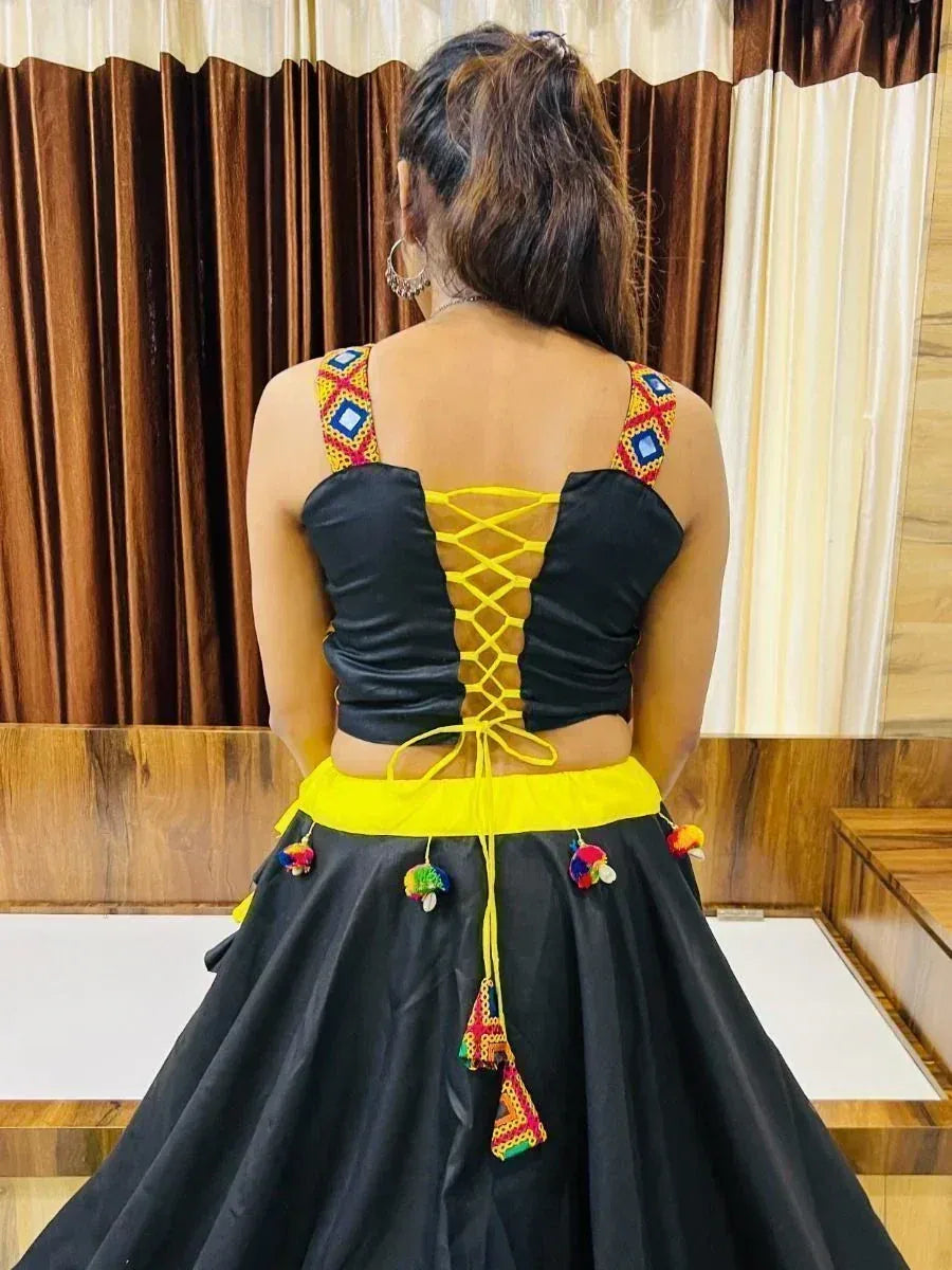 Black and yellow ethnic lehenga choli with lace-up back and colorful pom-poms, perfect for festive occasions.