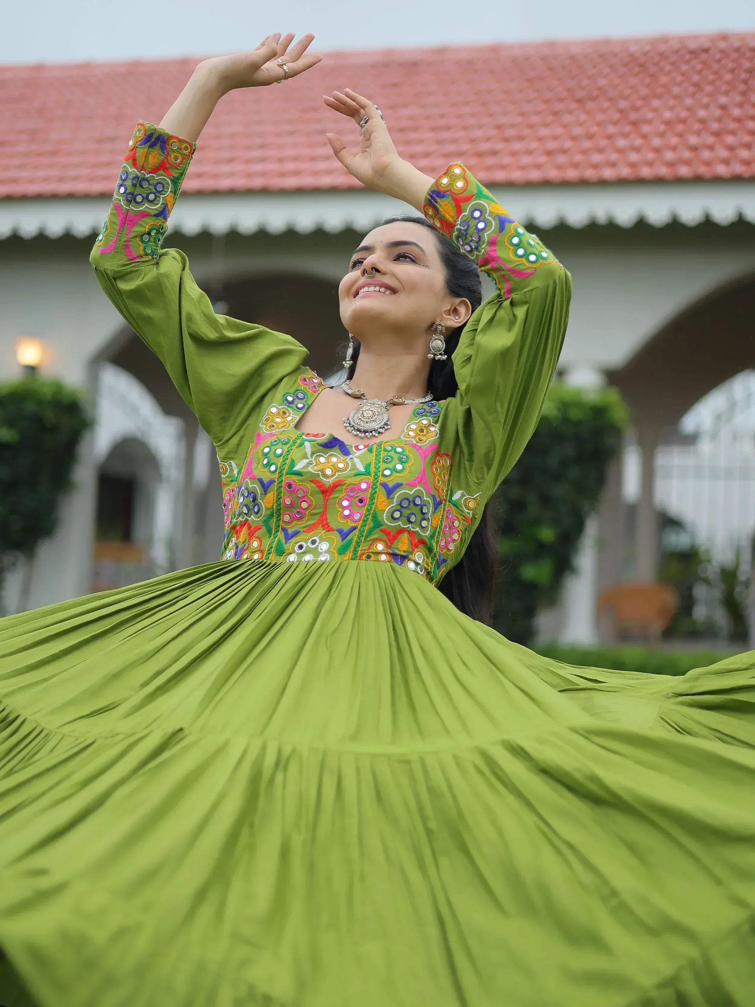Woman in vibrant green embroidered ethnic gown with mirror work, twirling outdoors