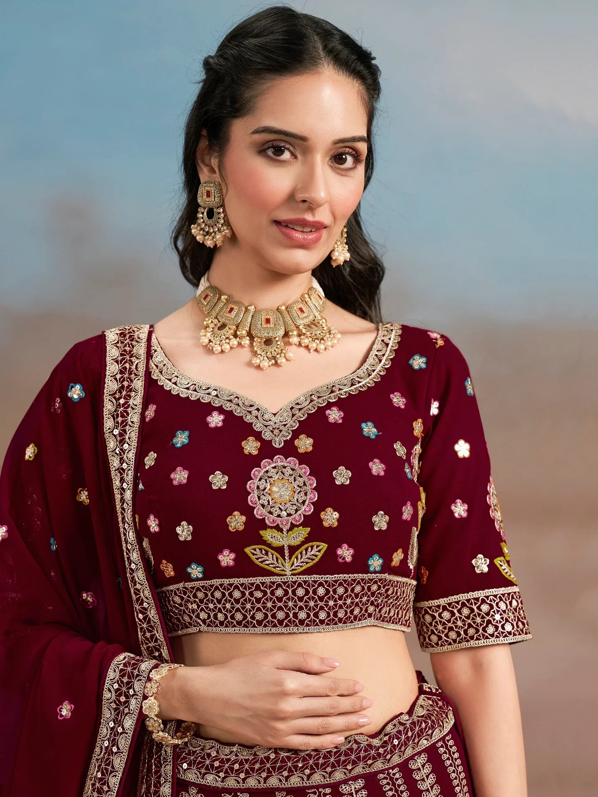 Maroon embroidered lehenga choli with floral motifs and gold jewelry, perfect for Indian ethnic wear occasions.