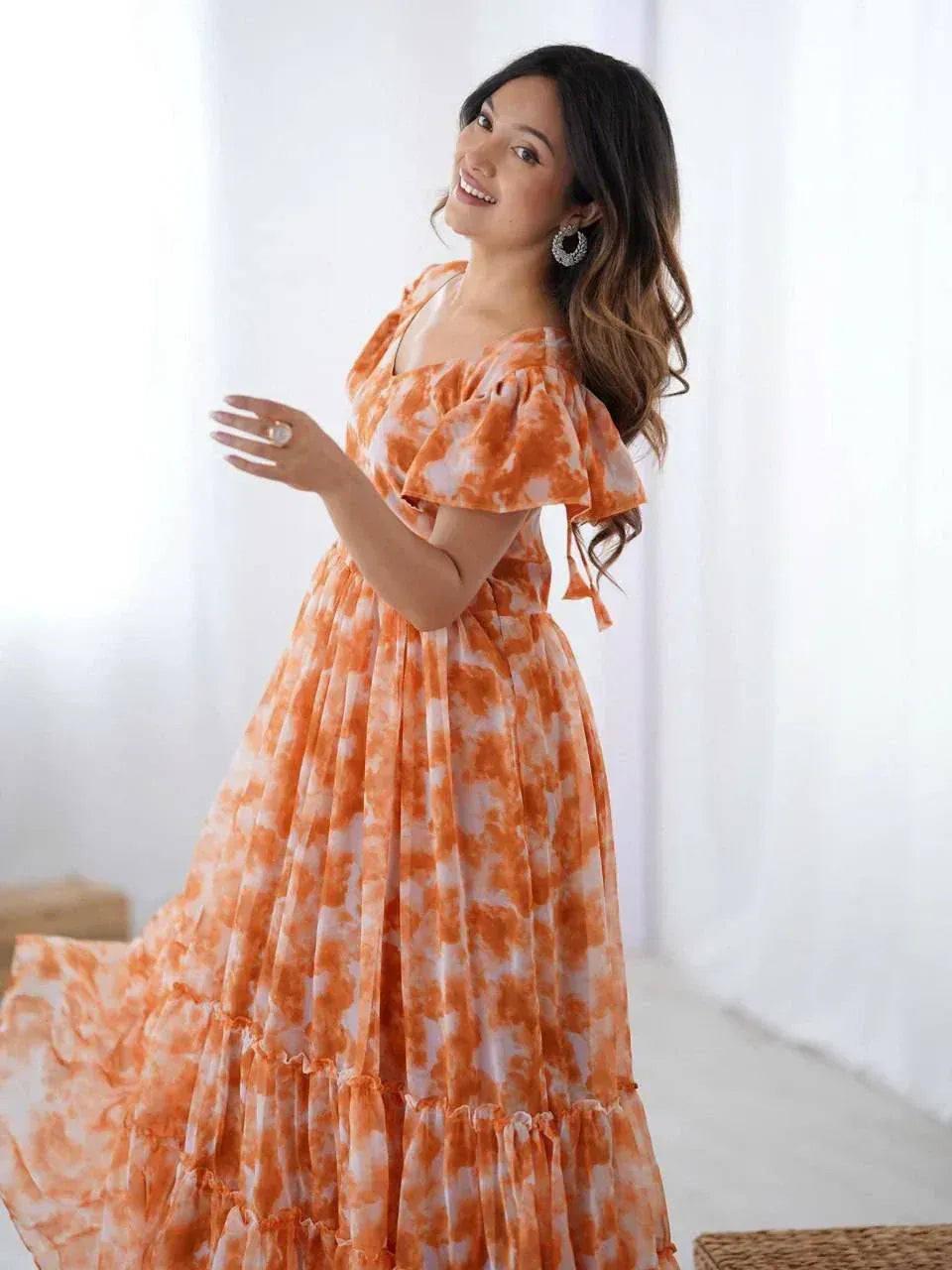 Woman in an orange tie-dye ethnic gown with ruffled sleeves, posing indoors