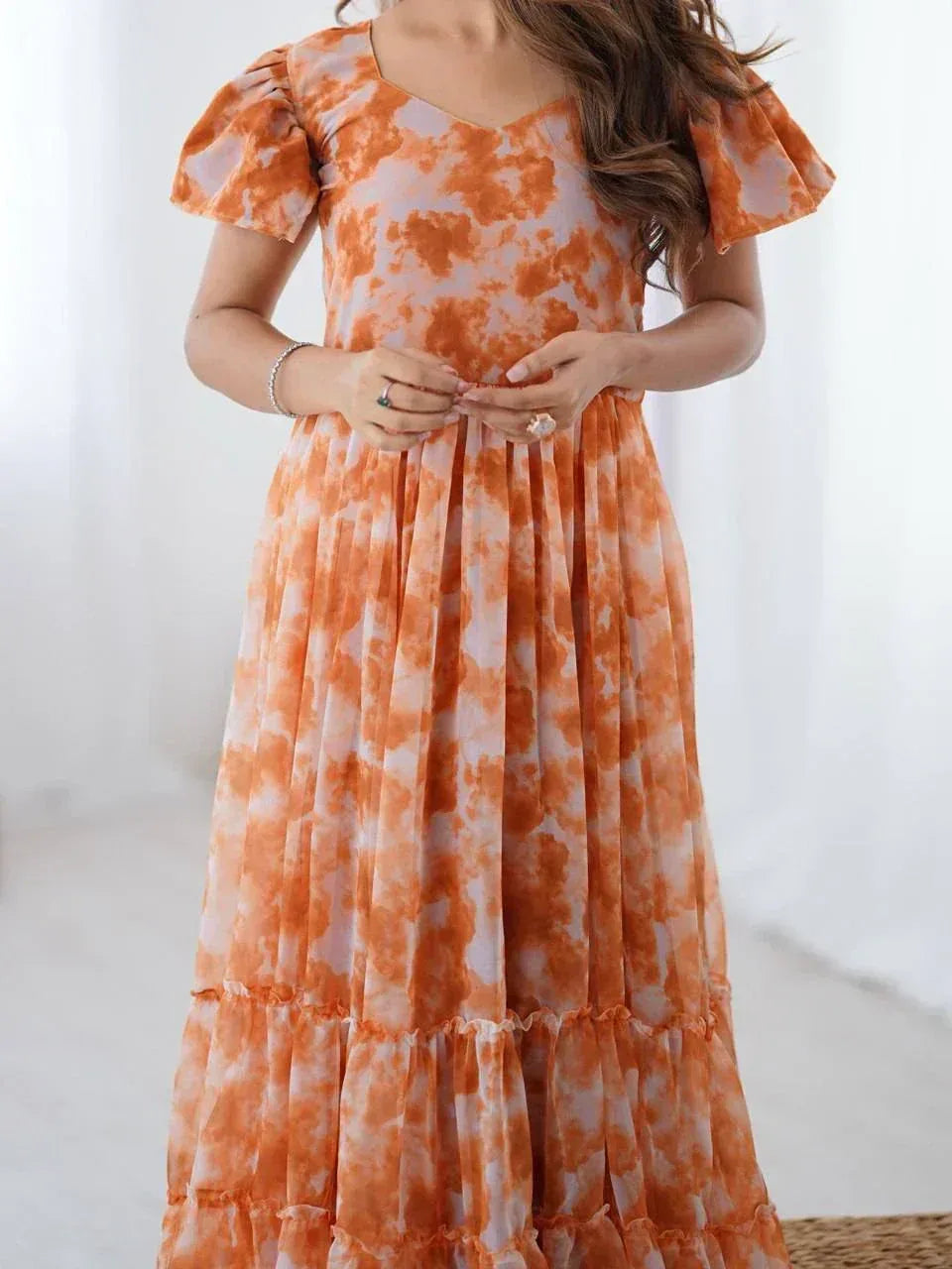 Woman wearing orange tie-dye ethnic gown with flutter sleeves in a bright room