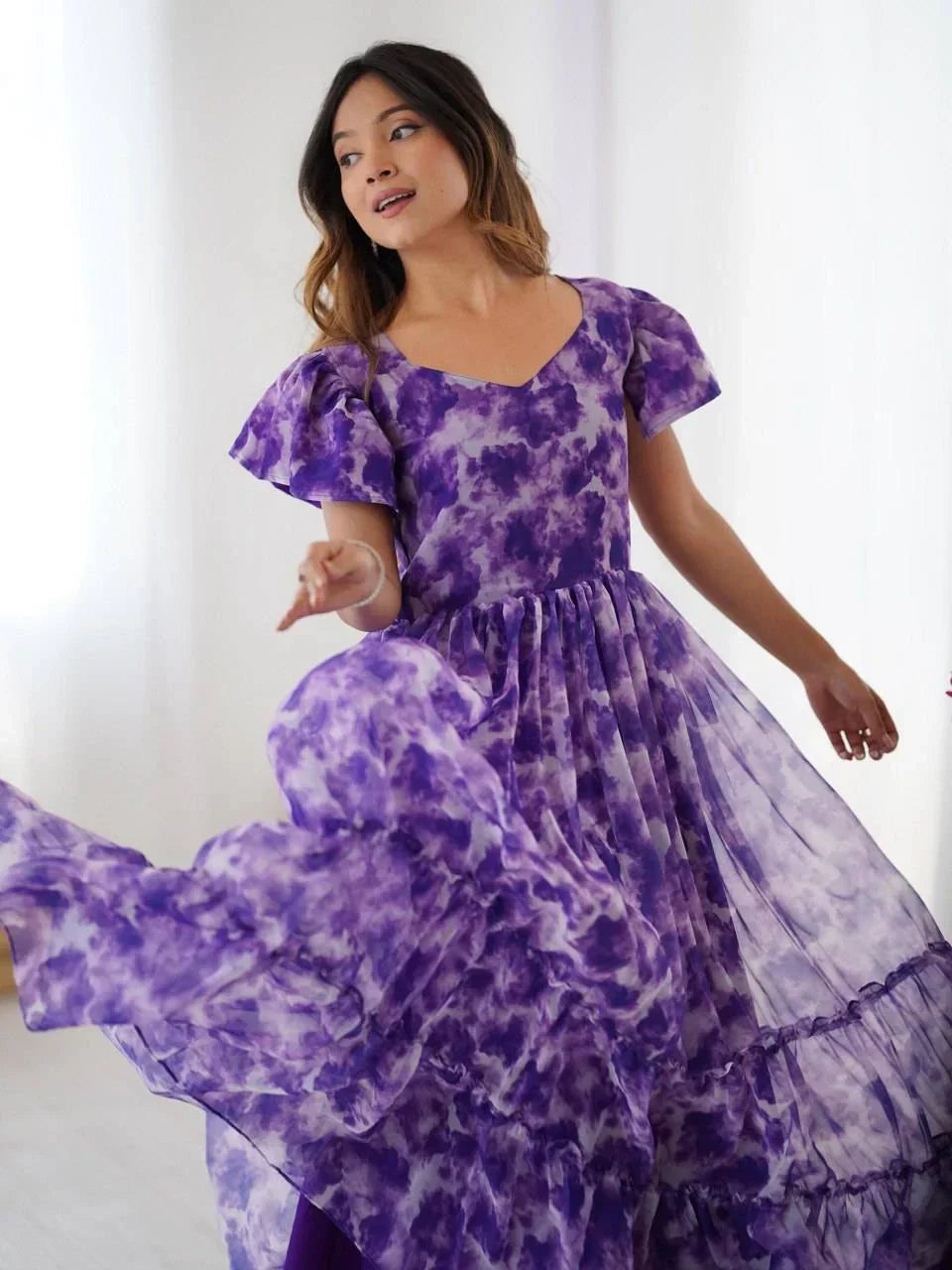 Woman in flowing purple floral ethnic gown with flutter sleeves posing indoors