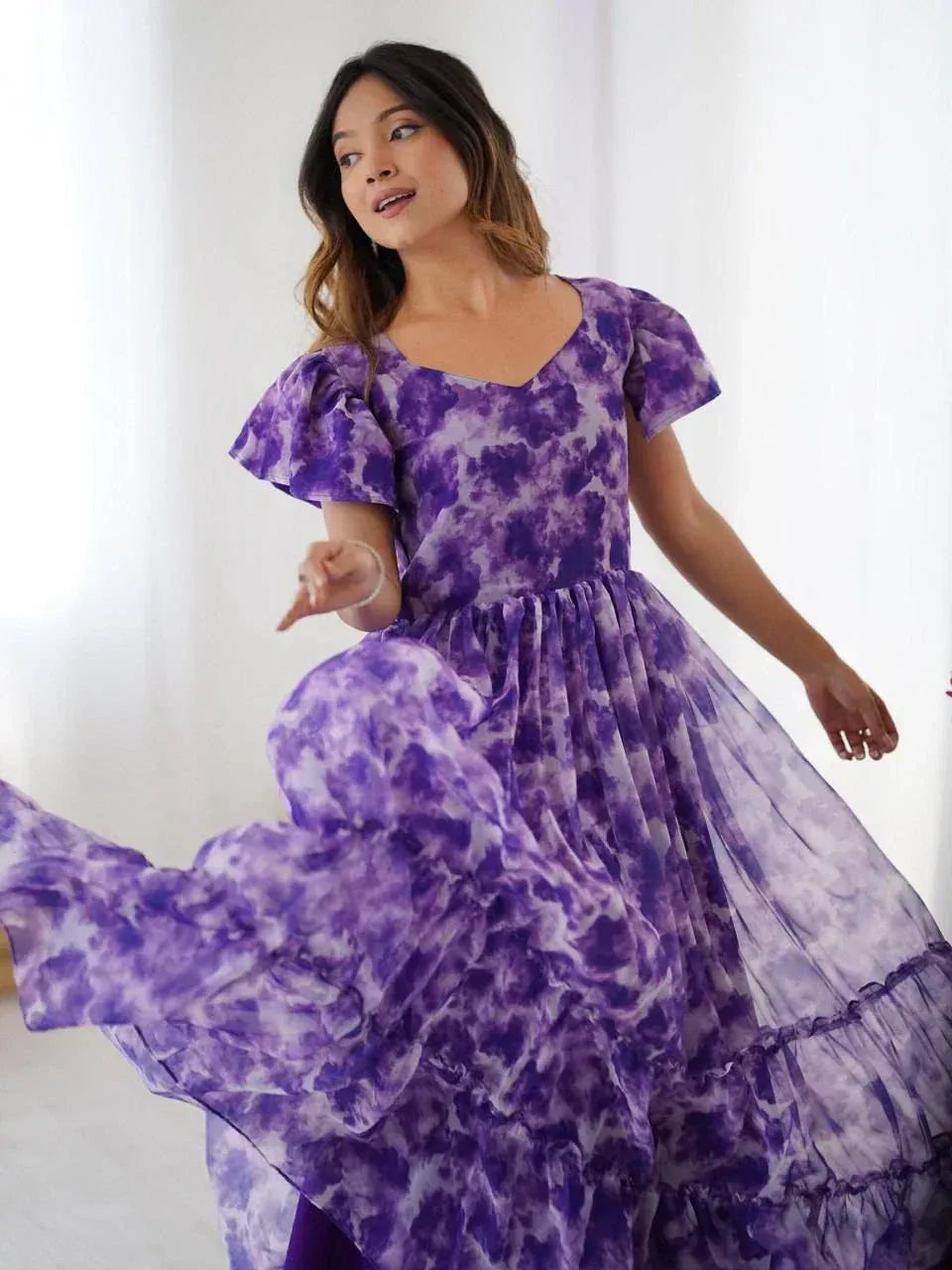Woman in flowing purple floral ethnic gown with flutter sleeves posing indoors