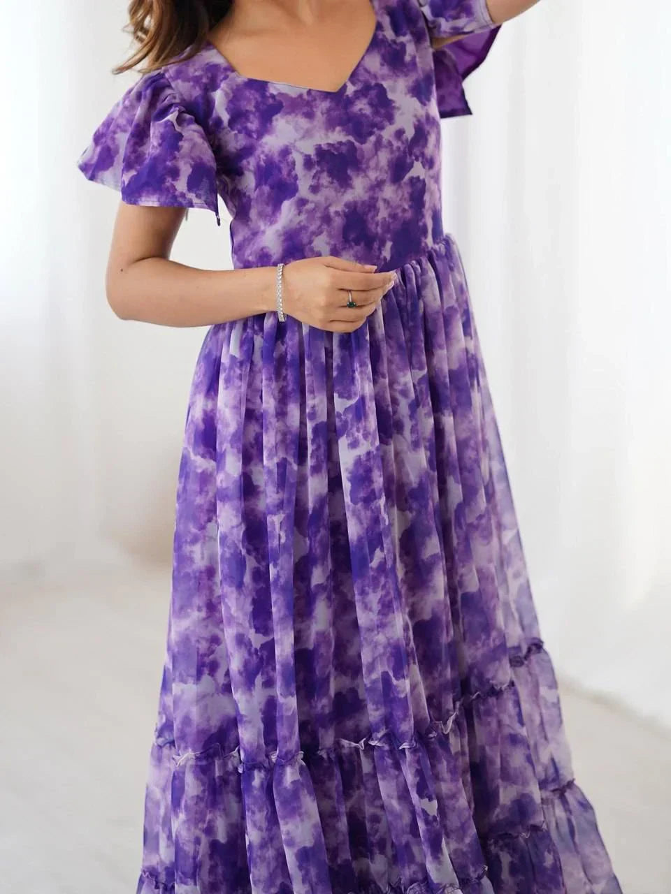 Woman wearing a purple tie-dye ethnic gown with flutter sleeves, standing indoors