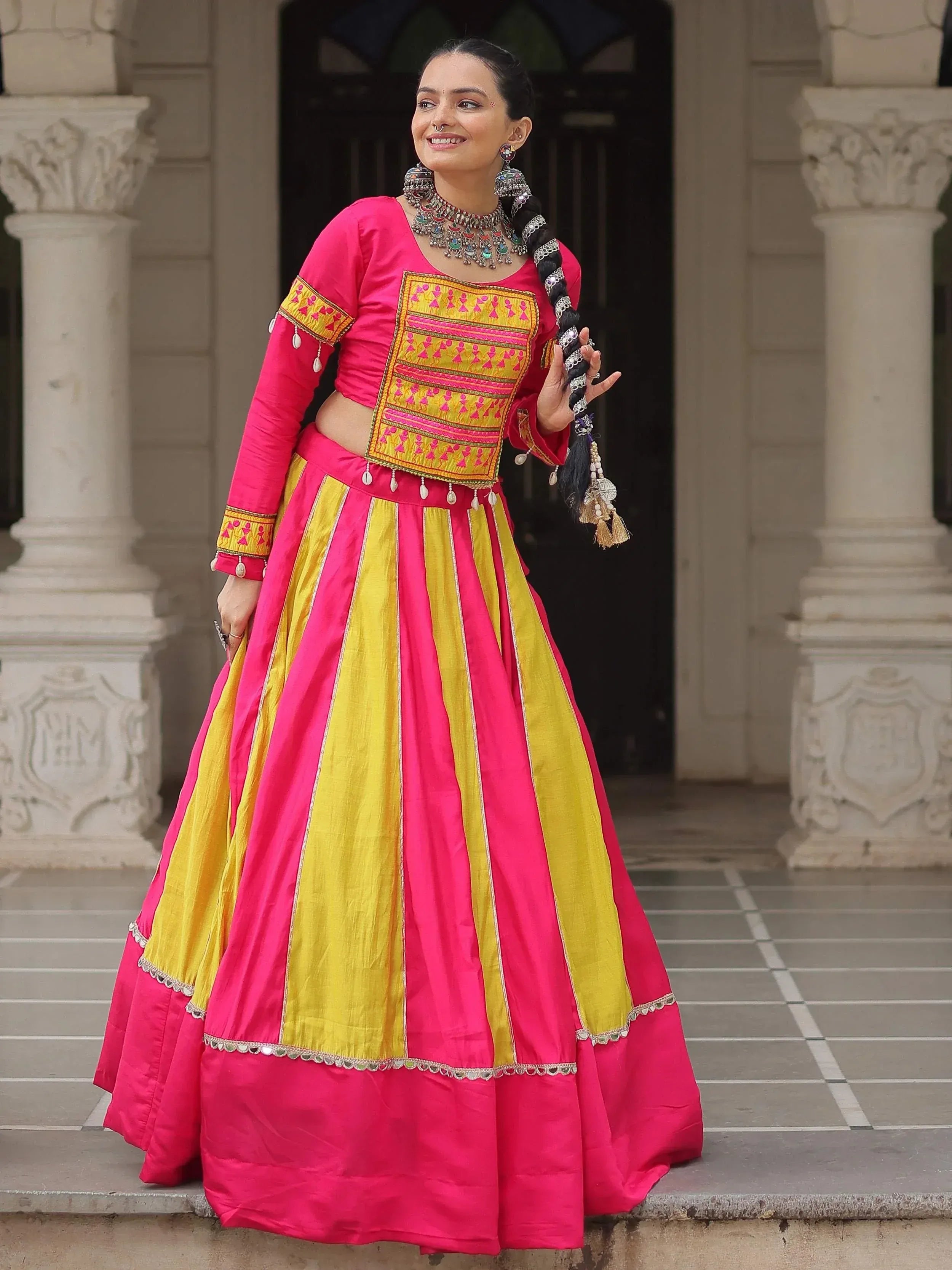 Vibrant pink and yellow ethnic lehenga choli with intricate embroidery and traditional jewelry