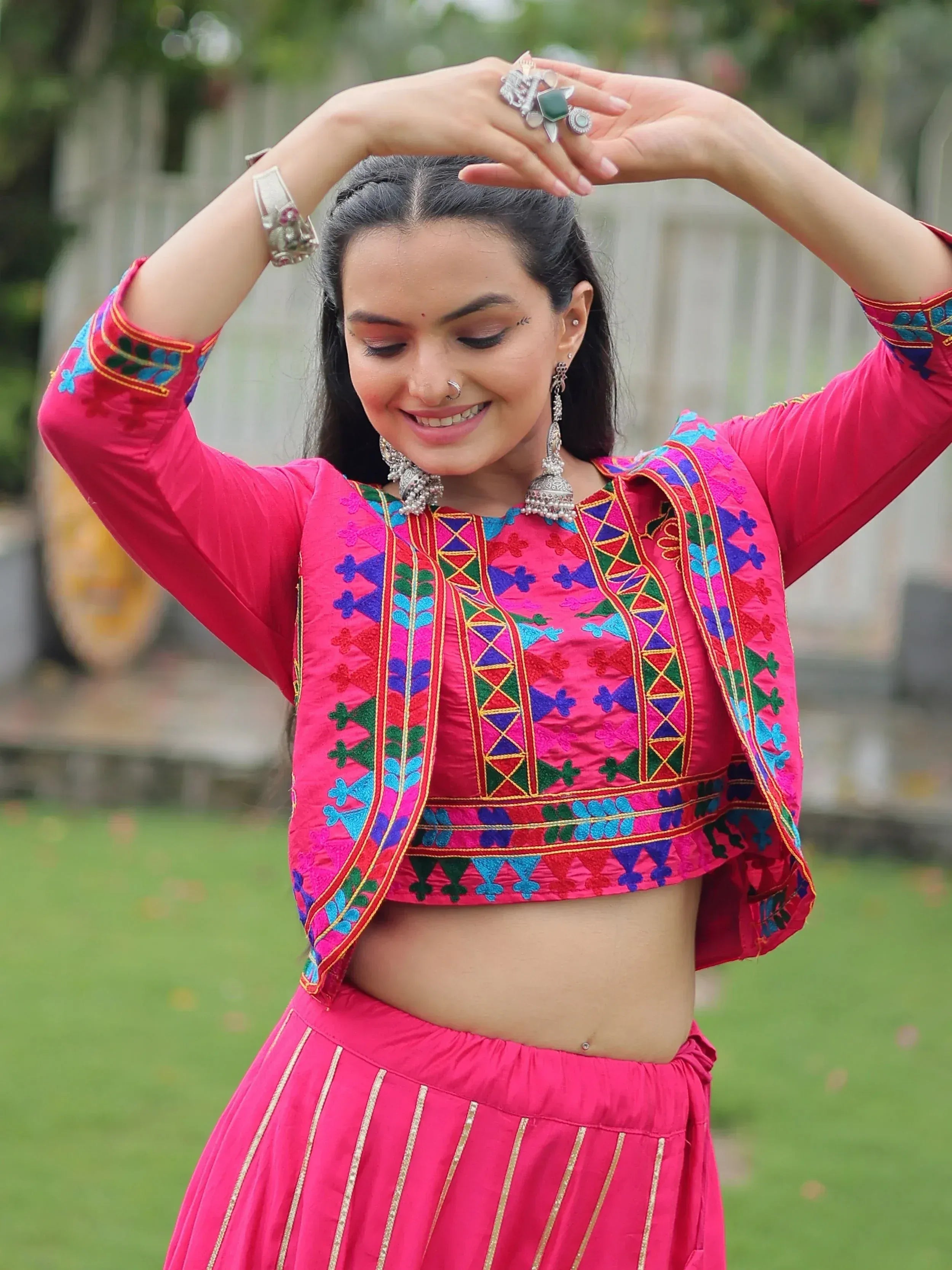 Vibrant pink embroidered ethnic crop top and skirt set with traditional jewelry, perfect for festive occasions.
