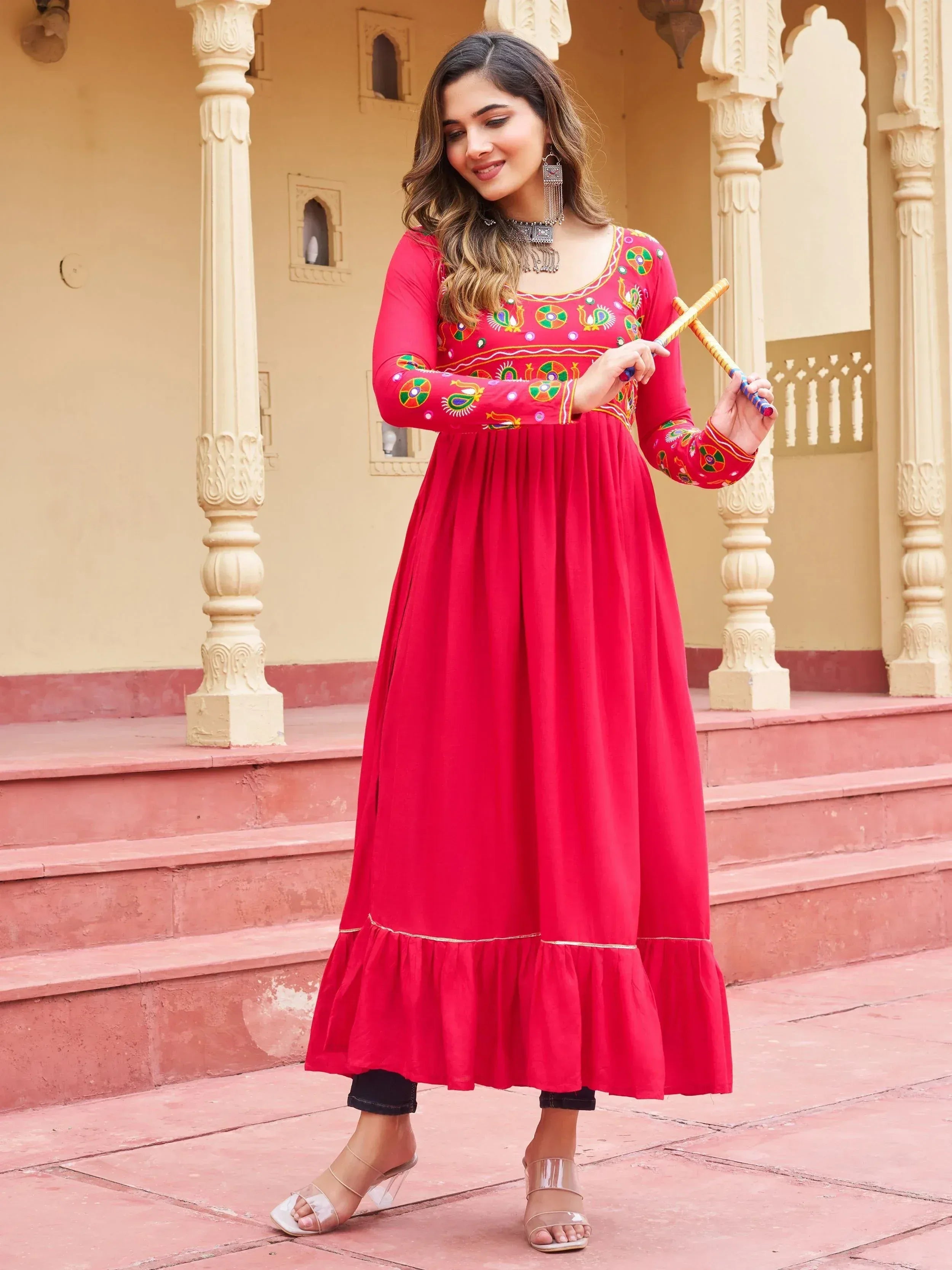 Red embroidered ethnic gown with ruffled hem, styled with traditional accessories and sandals.