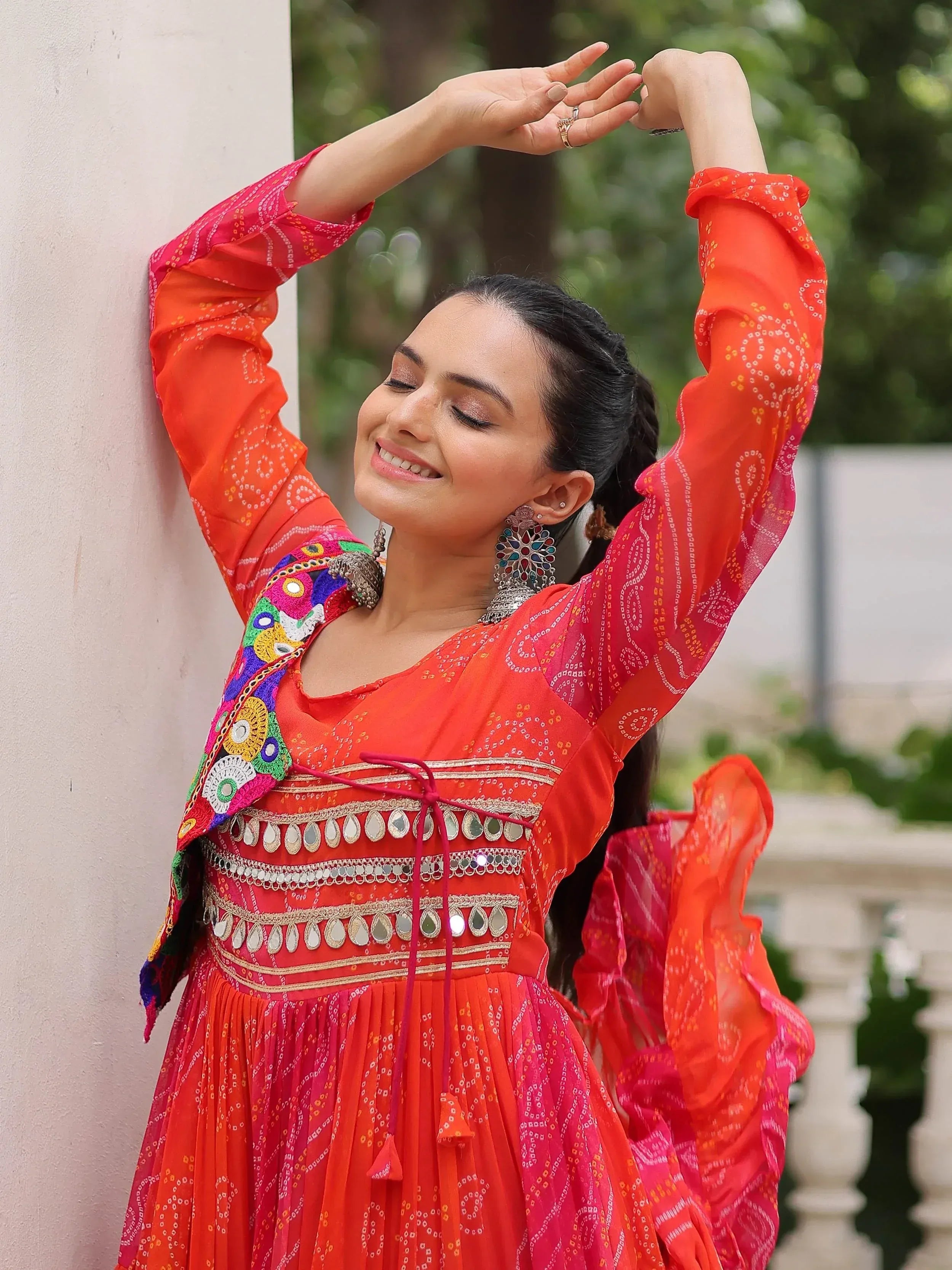 Woman in vibrant orange and pink ethnic gown with mirror work, perfect for Indian festive occasions.