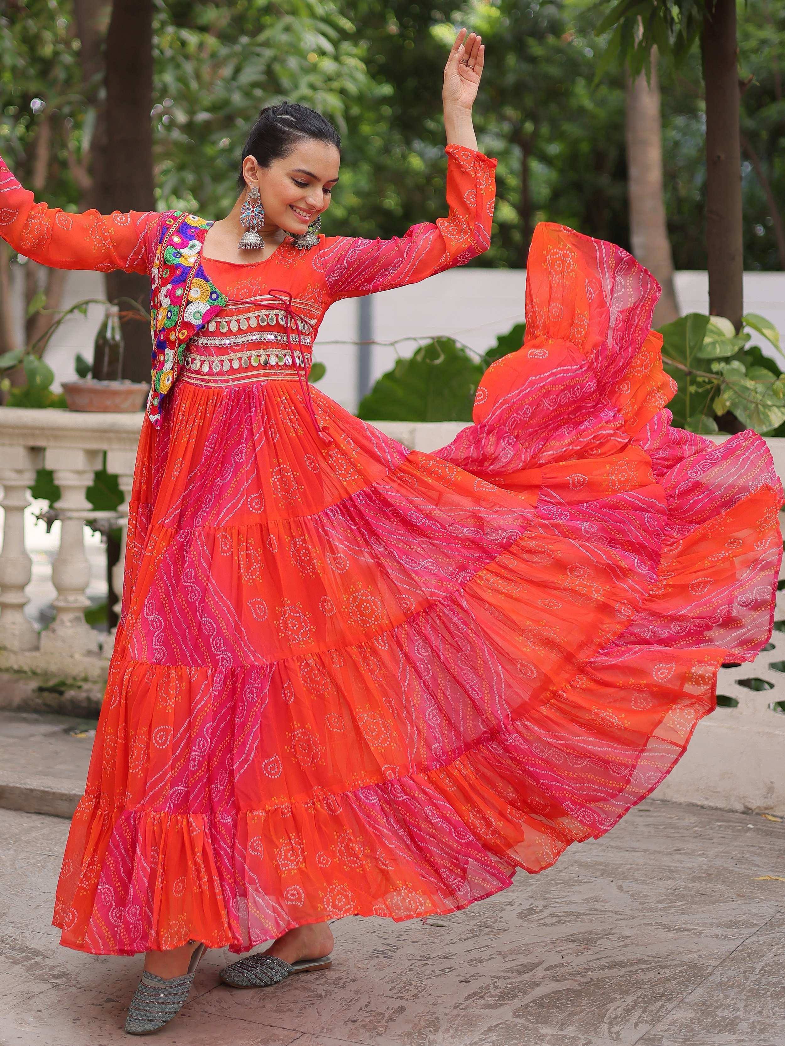 Woman twirling in vibrant orange and pink ethnic gown with mirror work, perfect for festive occasions.